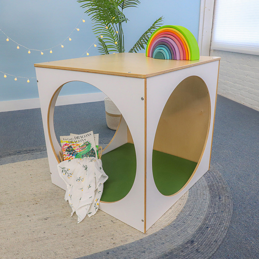 Children's play cube with green mat and rainbow toy in a room setting.