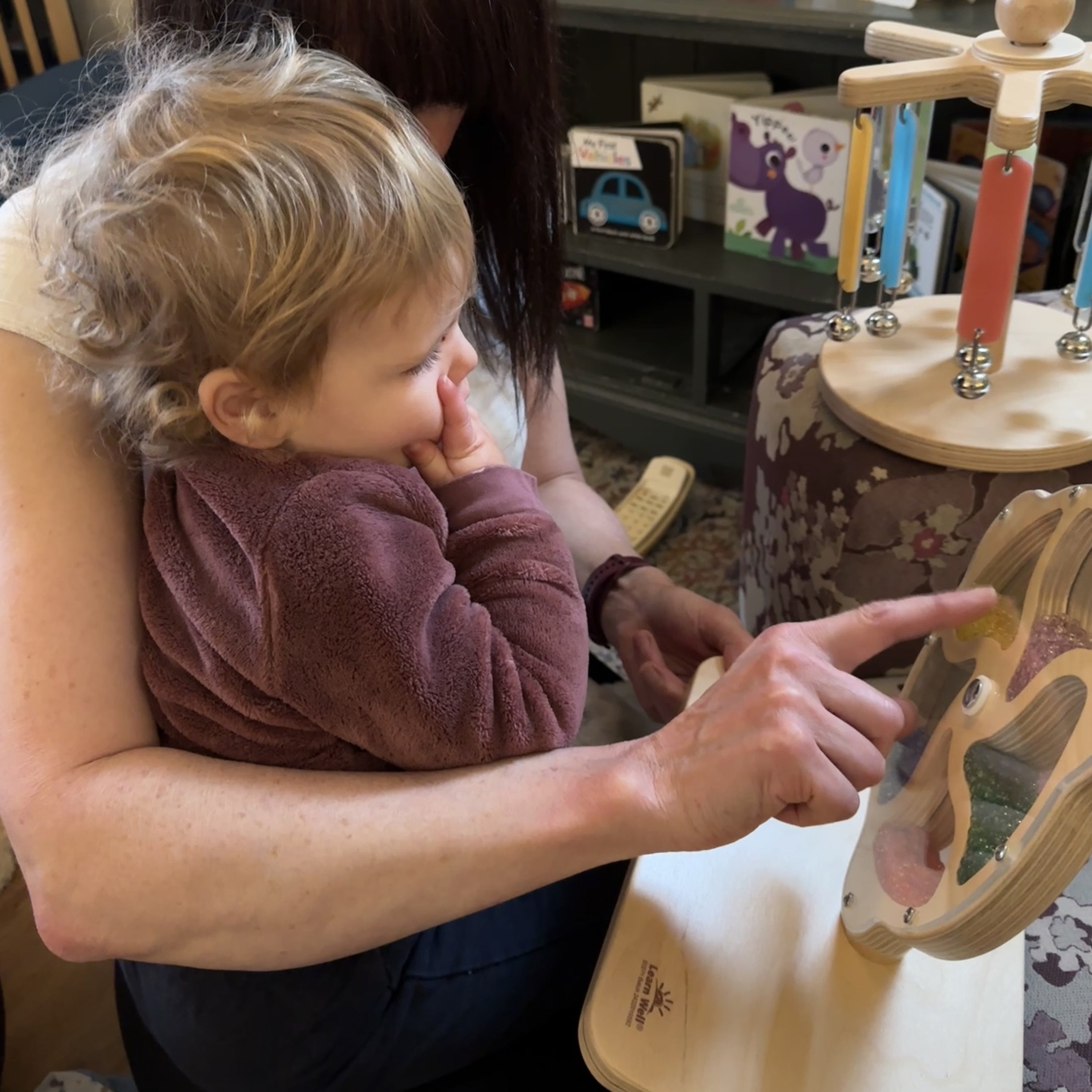 Child being held by an adult in a home setting with toys and books in the background