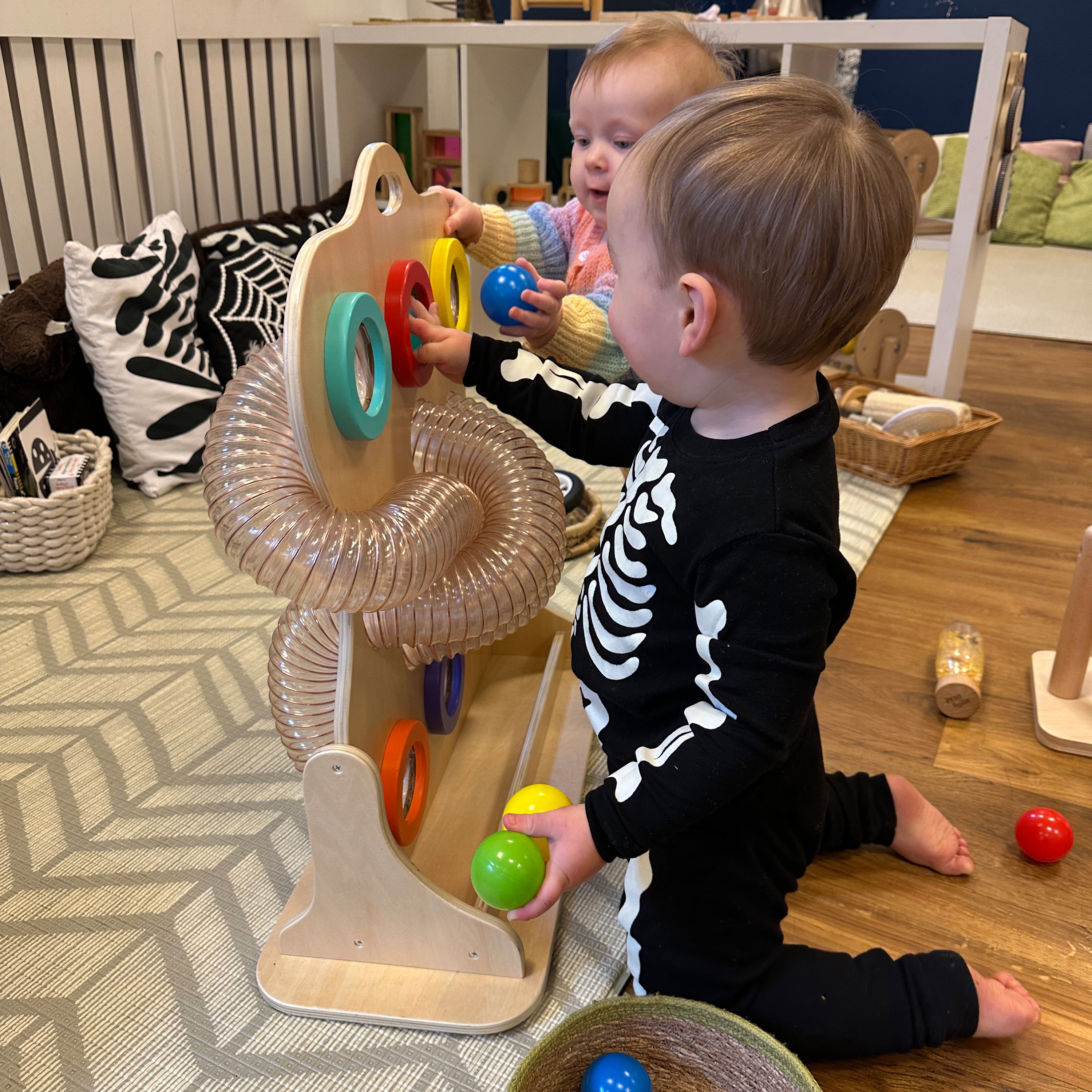 Two children playing with a colorful toy on a wooden floor.
