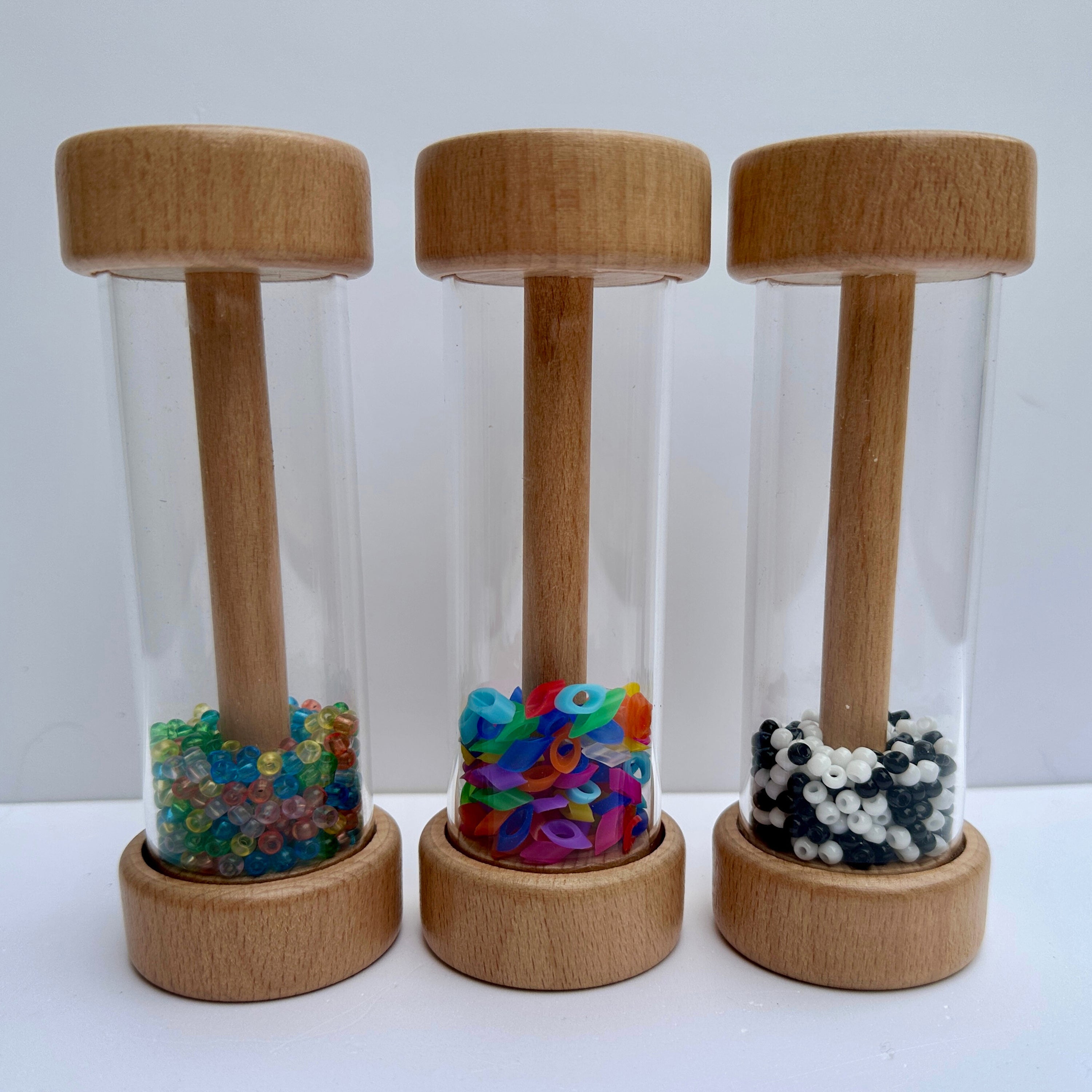 Three plastic tubes with wooden lids and bases, each filled with colorful beads on a white background.