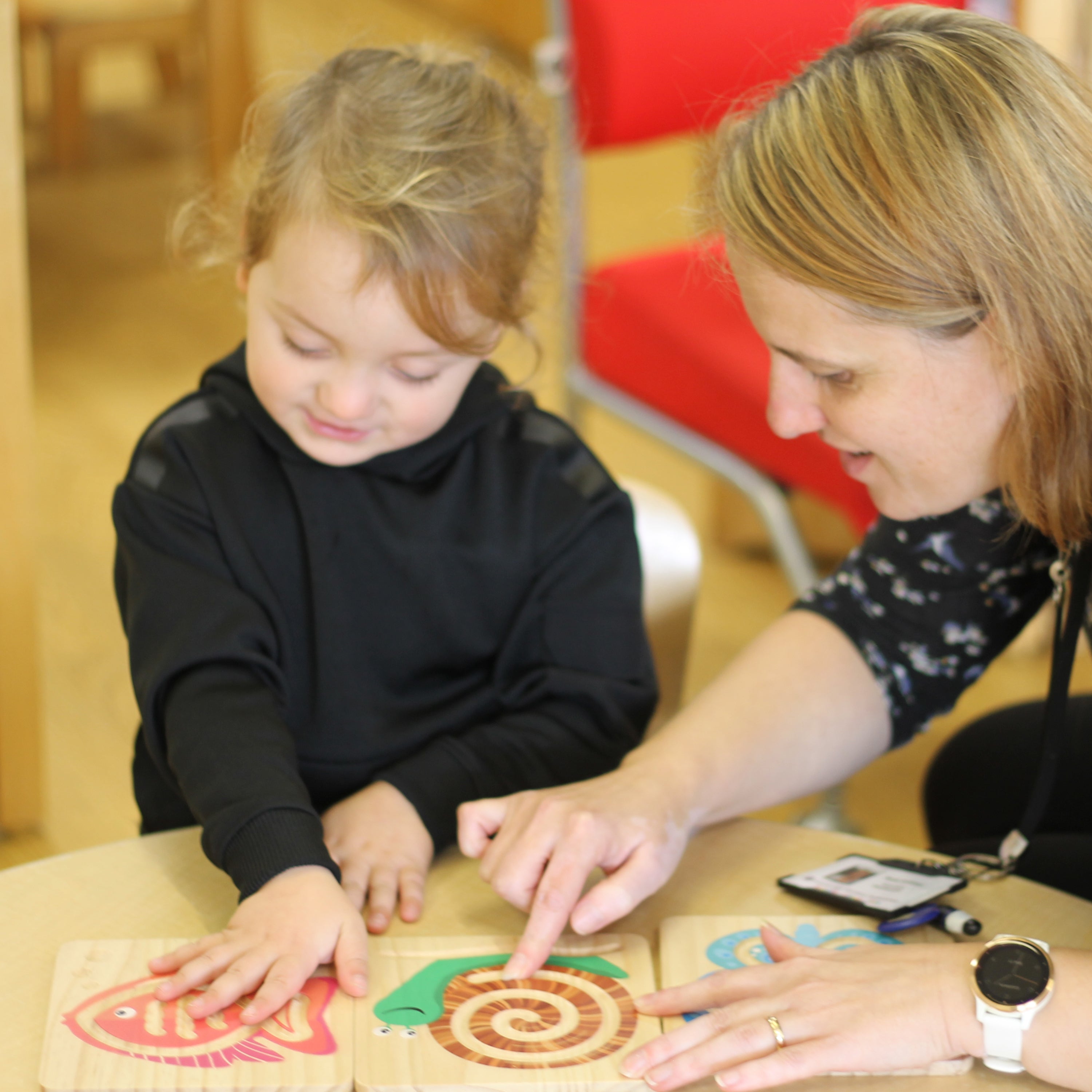 Child and adult interacting with wooden puzzle pieces on a table.