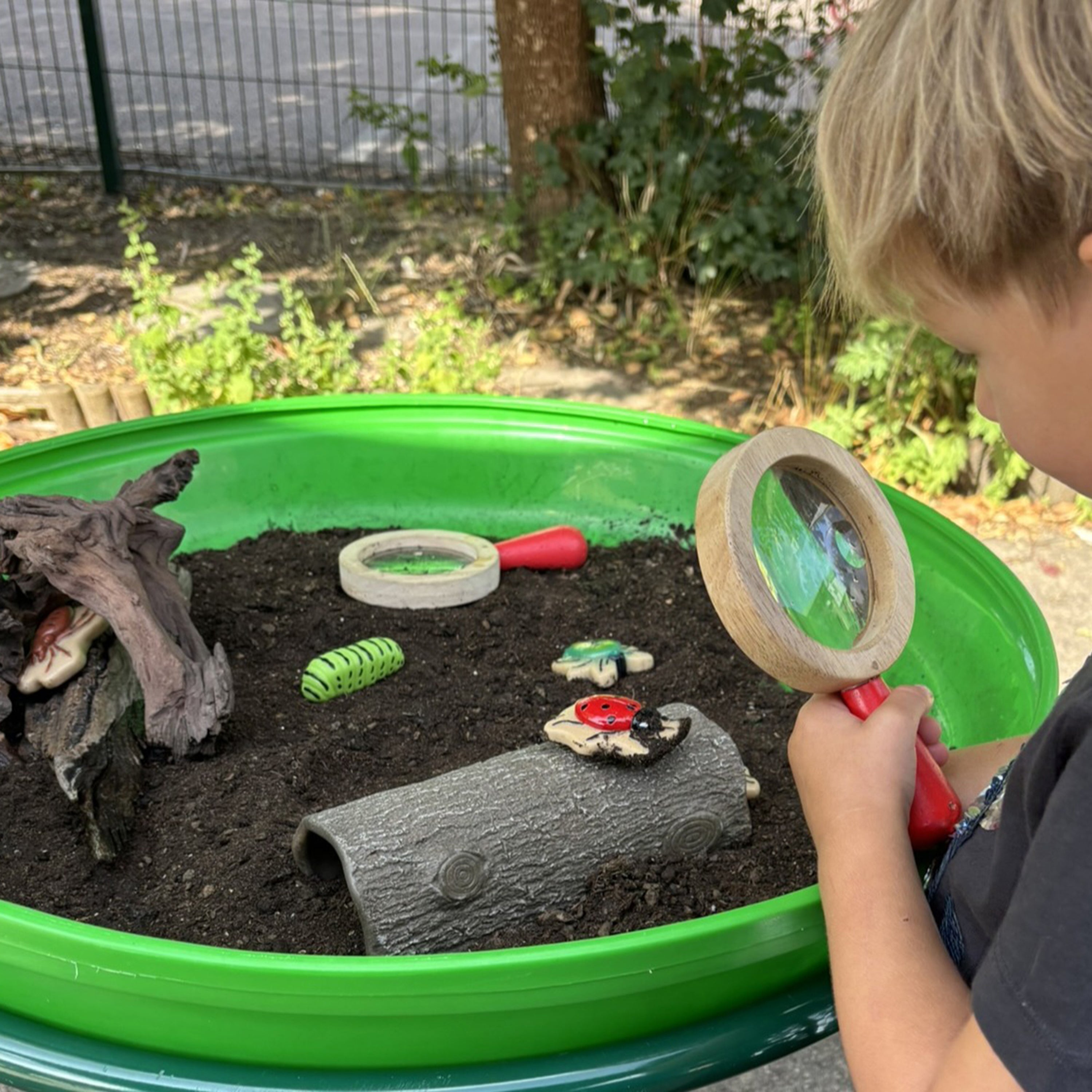 Child examining outdoor play setup with magnifying glass