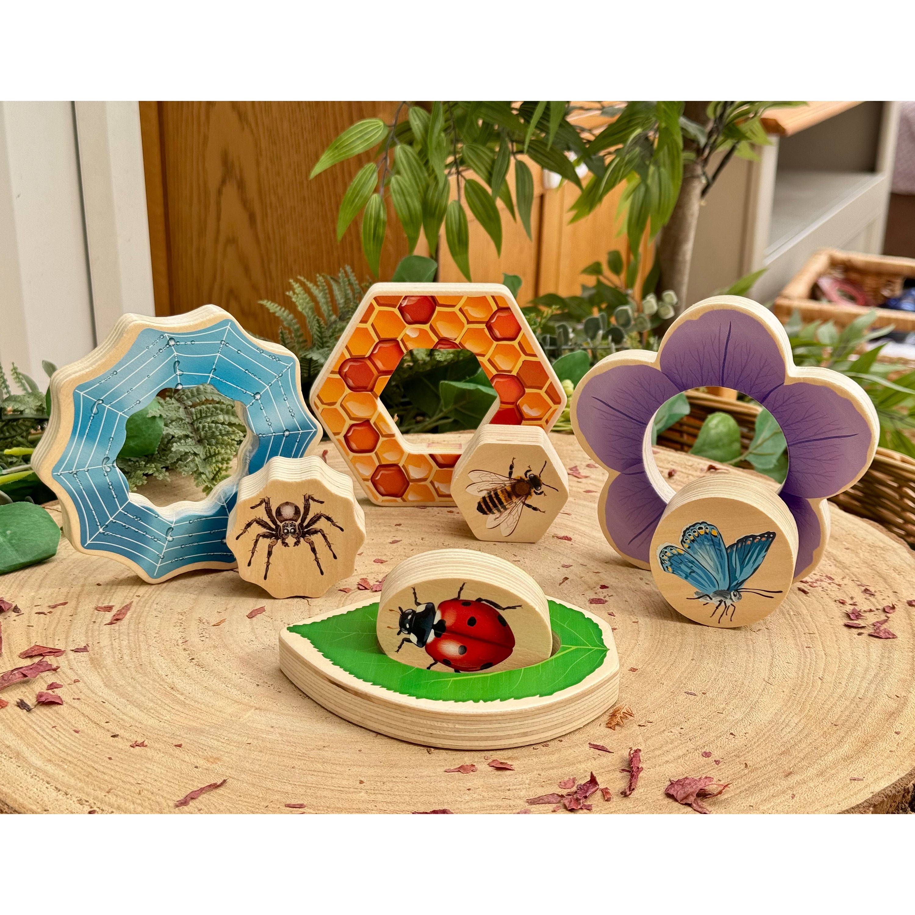 Set of wooden insect-themed toys on a wooden surface with plants in the background