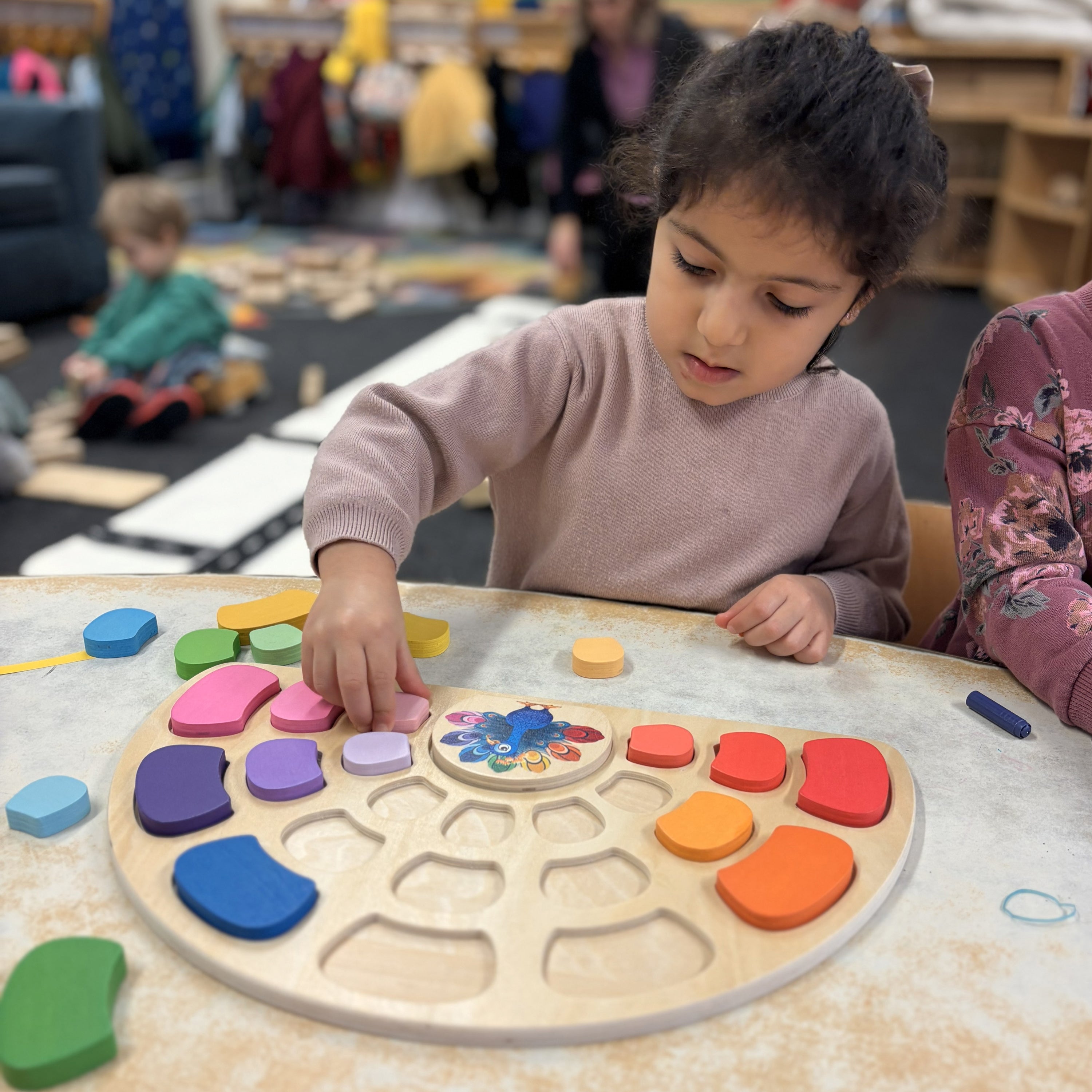 Child playing with a colorful puzzle at a table in a classroom setting.