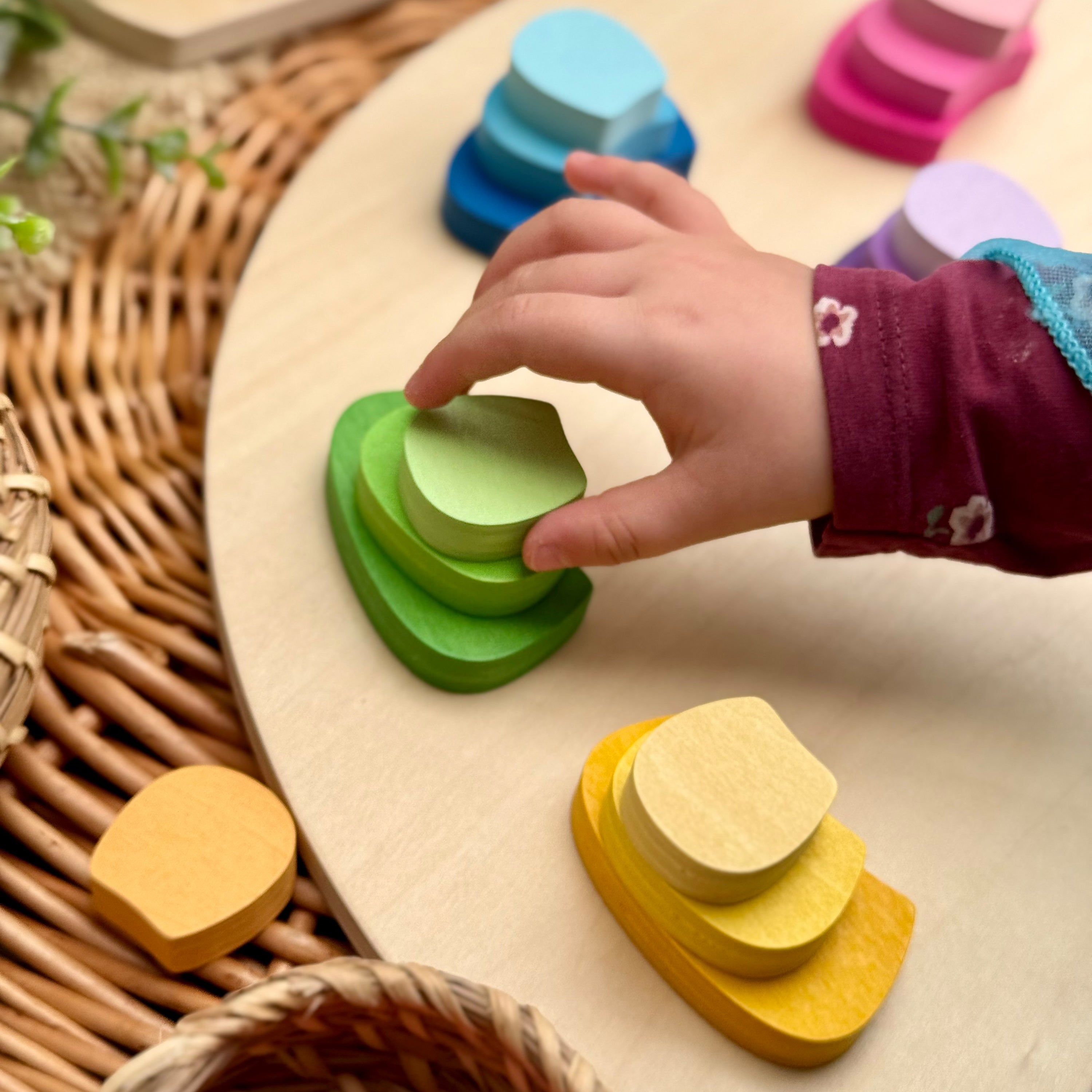 Child's hand interacting with colorful wooden stacking toys on a woven surface