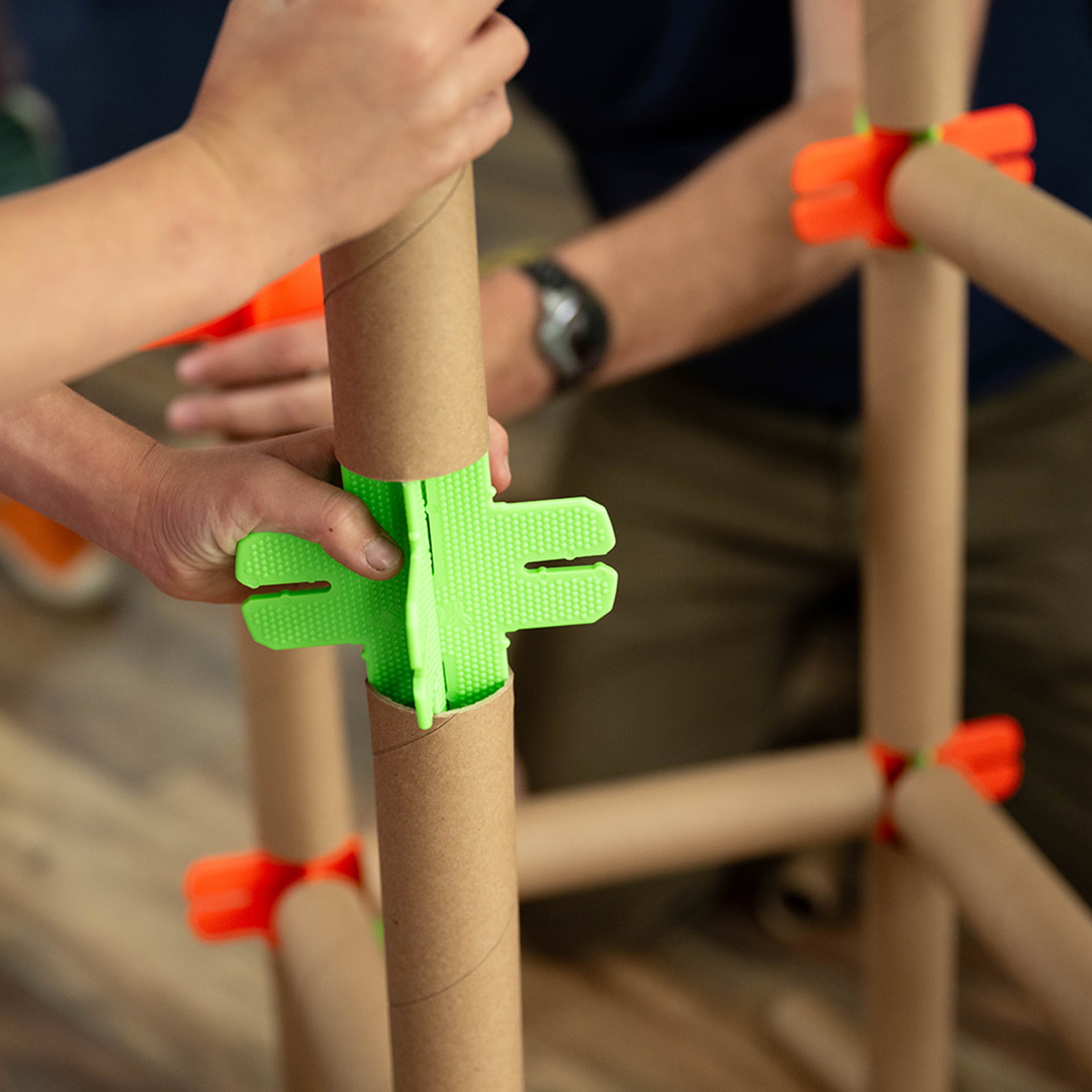 Close-up of hands using green tape to secure cardboard tubes together.