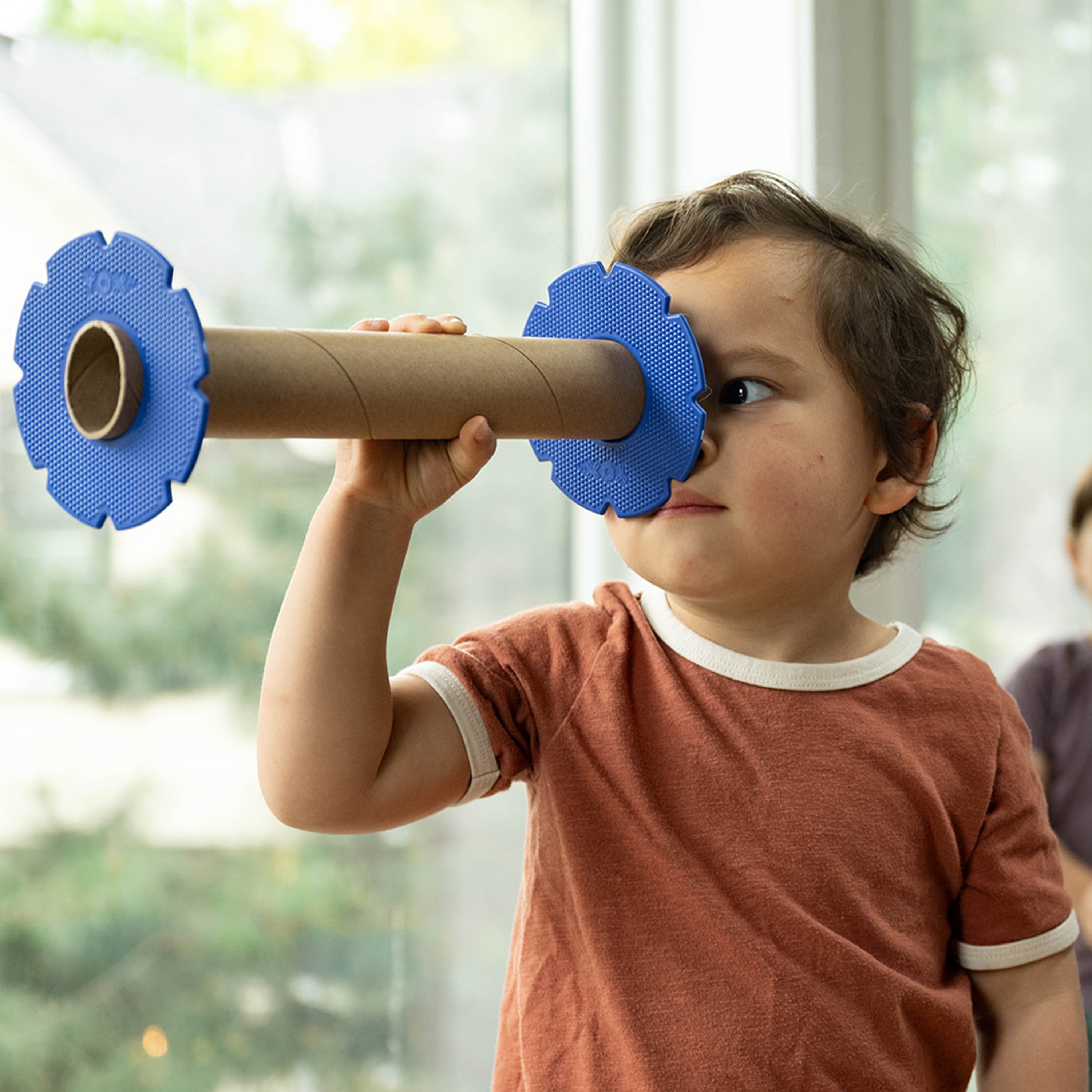 Child playing with a cardboard tube and blue foam pieces indoors