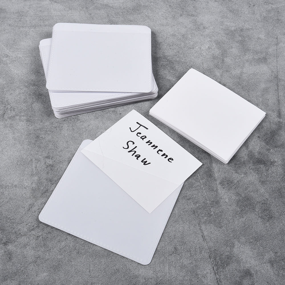 A stack of white adhesive labeling pockets on a grey surface, with one pocket displaying a written label.