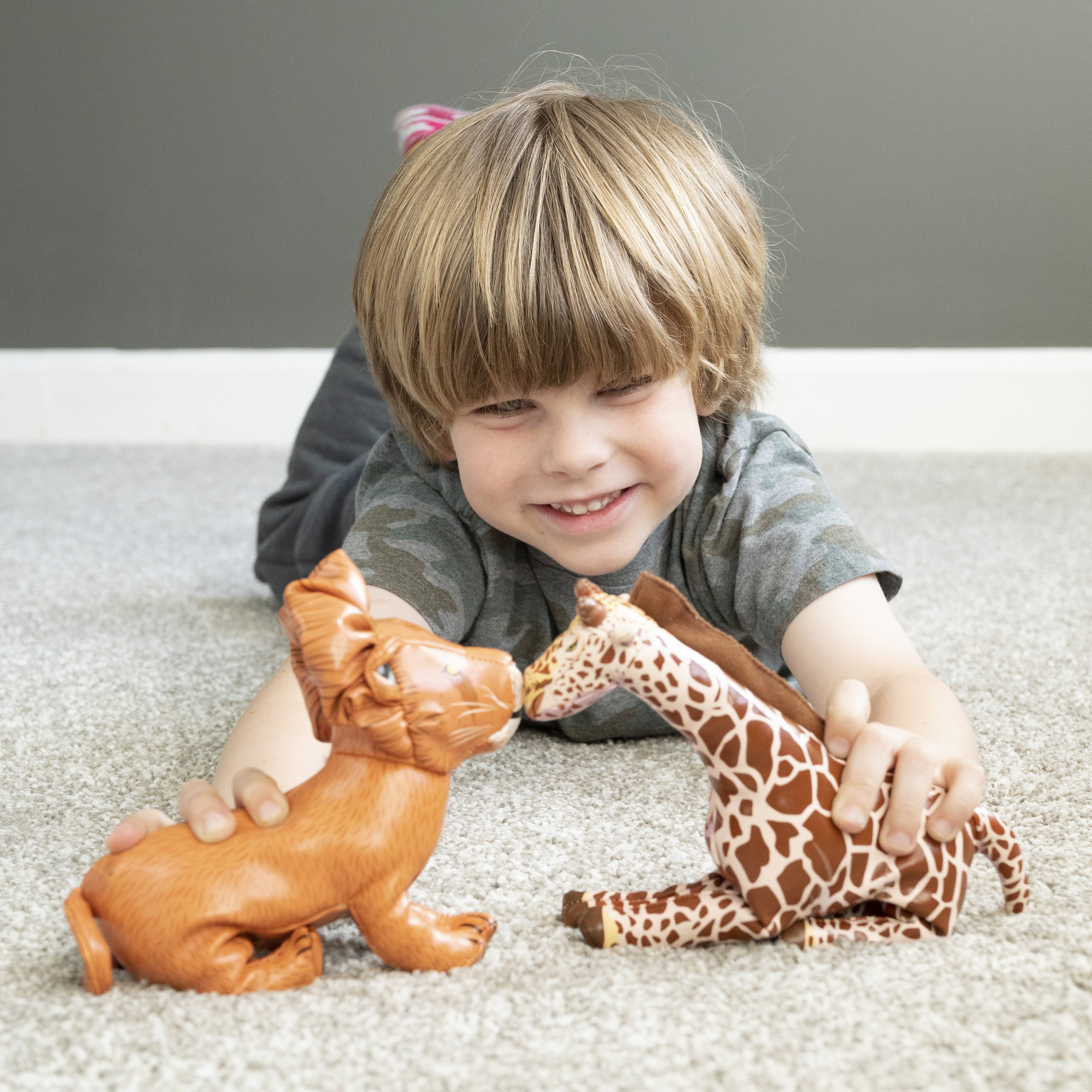 Boy on gray carpet playing with giraffe and lion animal figures