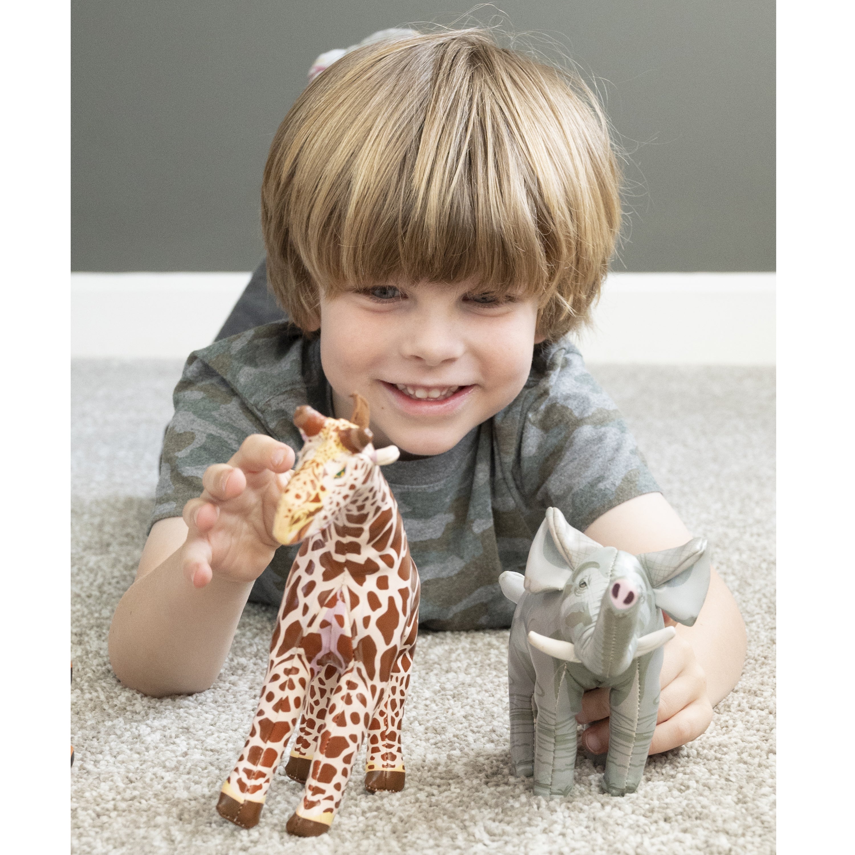 Boy on gray carpet playing with giraffe and elephant animal figures