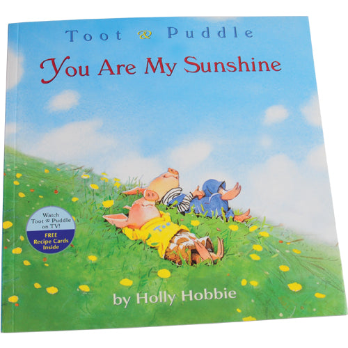 A children's book titled 'Toot & Puddle You Are My Sunshine' with an illustration of two cartoon piggies and a human character on a grassy field with flowers and a blue sky in the background.