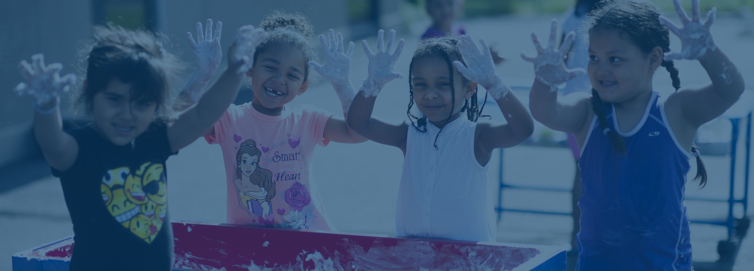 four children hold their hands up and smile as they play at the sensory and water table outside