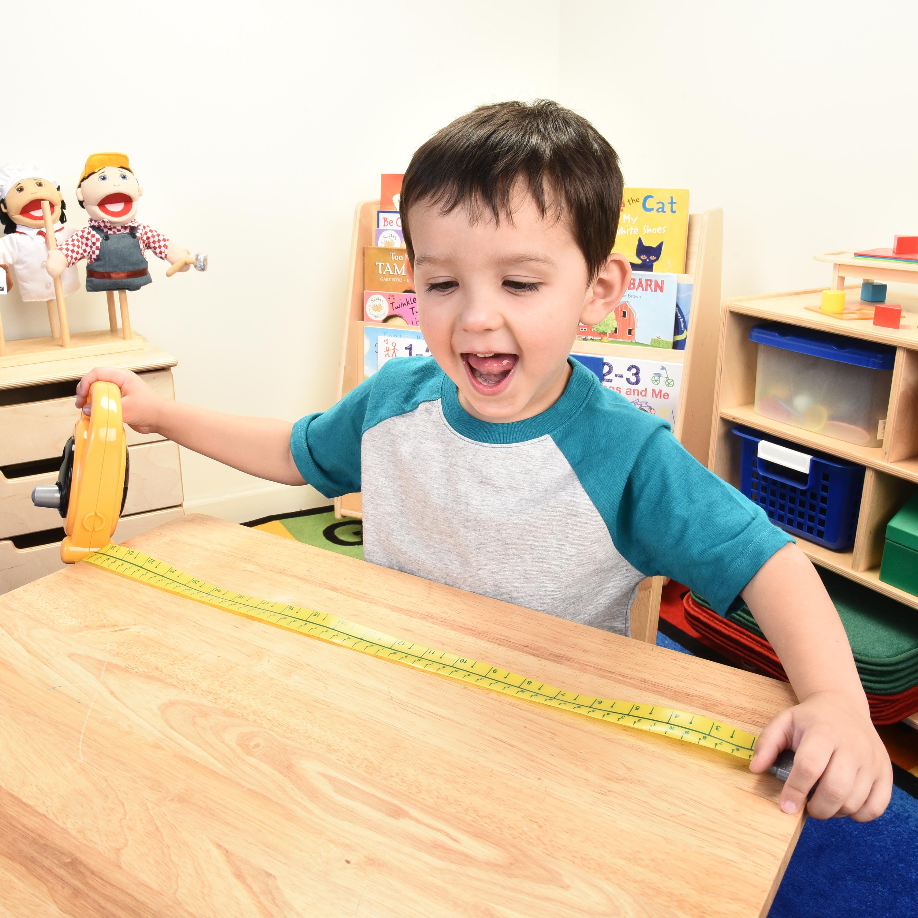 Child playing with a toy tape measure at a table in a classroom setting.