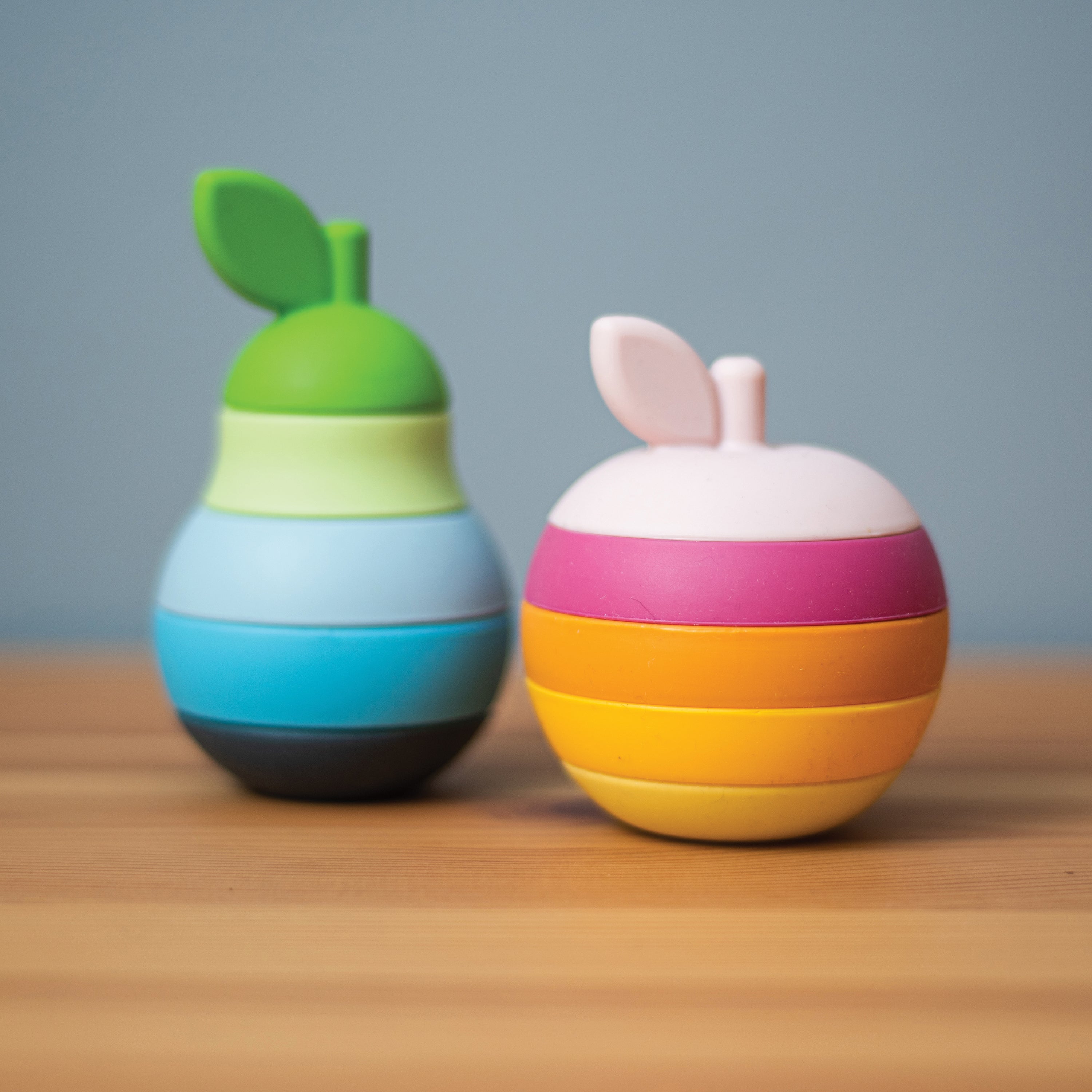 Two colorful toys resembling an apple and a pear on a wooden surface with a gray background