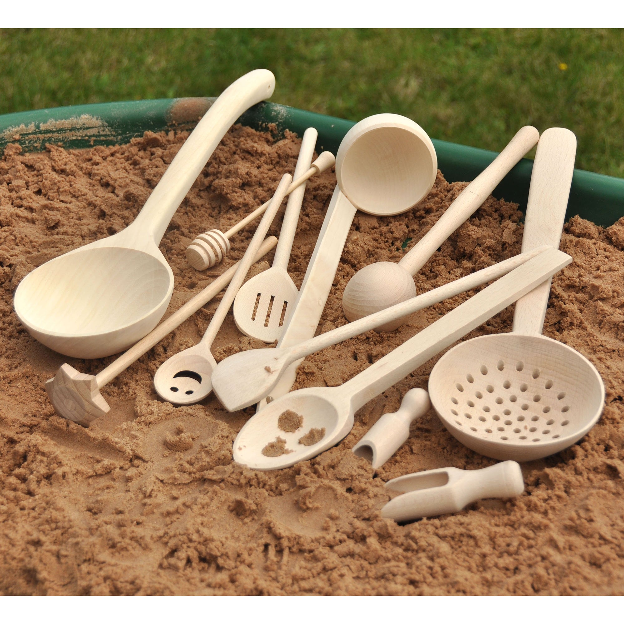 Set of white plastic kitchen utensils on a sandy surface with a green rimmed container.