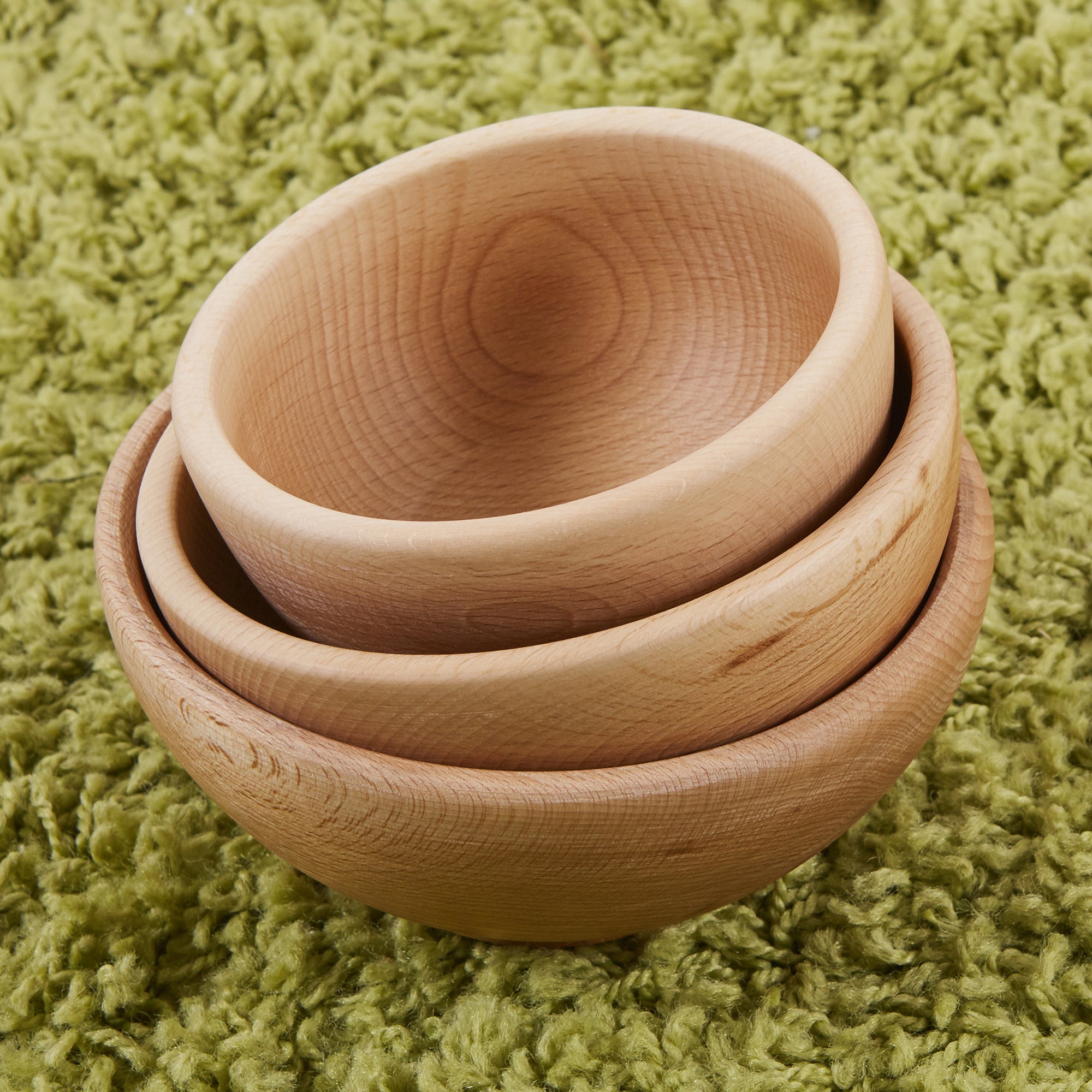 Stack of three wooden bowls on a green textured surface
