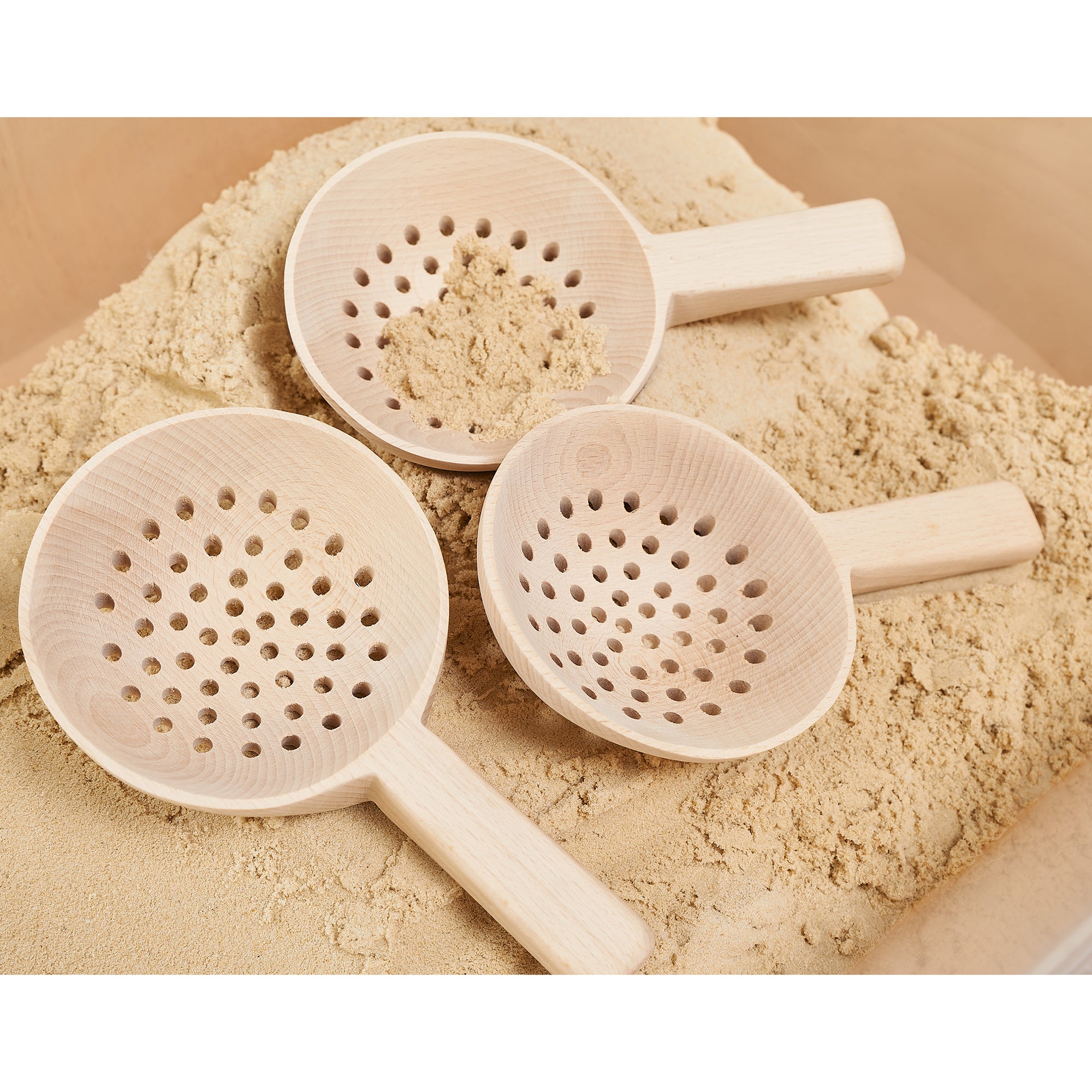 Three wooden sifting tools on a pile of sand with a beige background