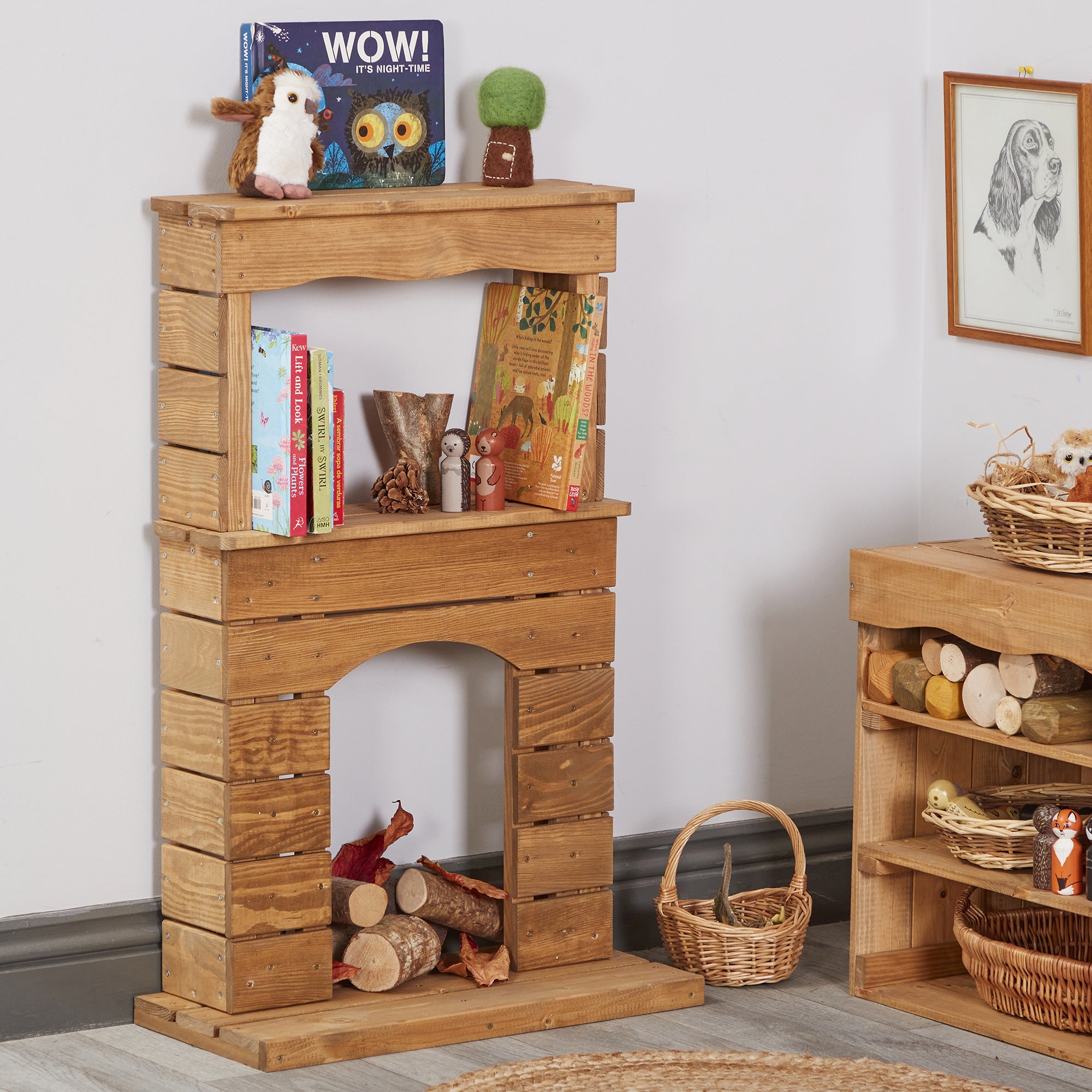 Wooden play fireplace with books and toys on a white wall background