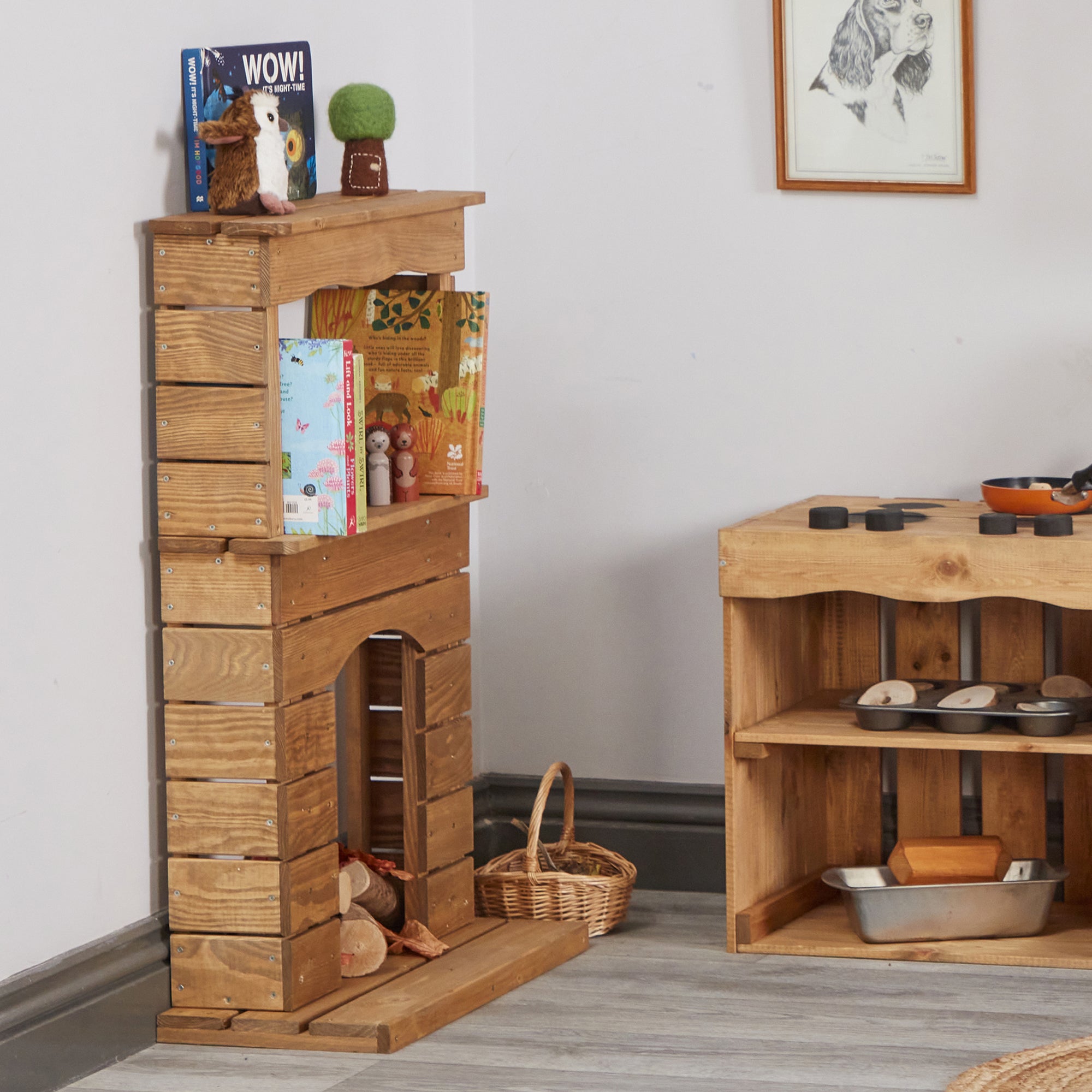 Wooden play kitchen set with shelves and toy items on a light gray floor.