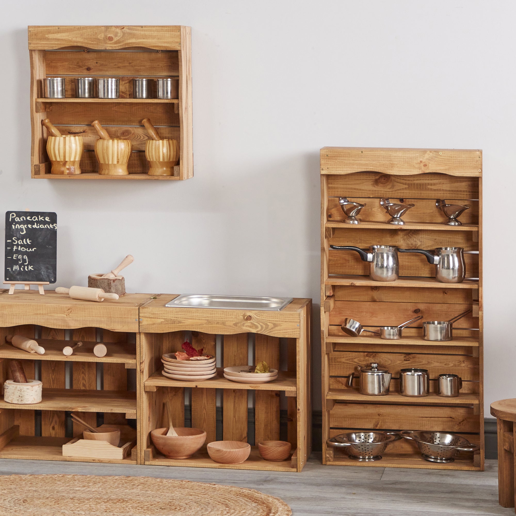 Wooden play kitchen furniture set with shelves and cooking utensils on a light gray background