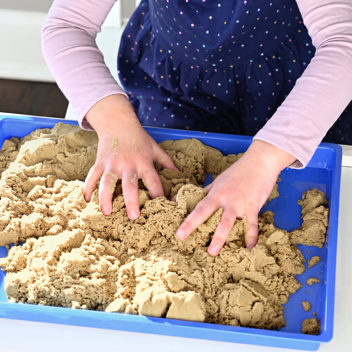 Child exploring Wonder Flow Sensory Sand in a blue sensory tray for hands-on play