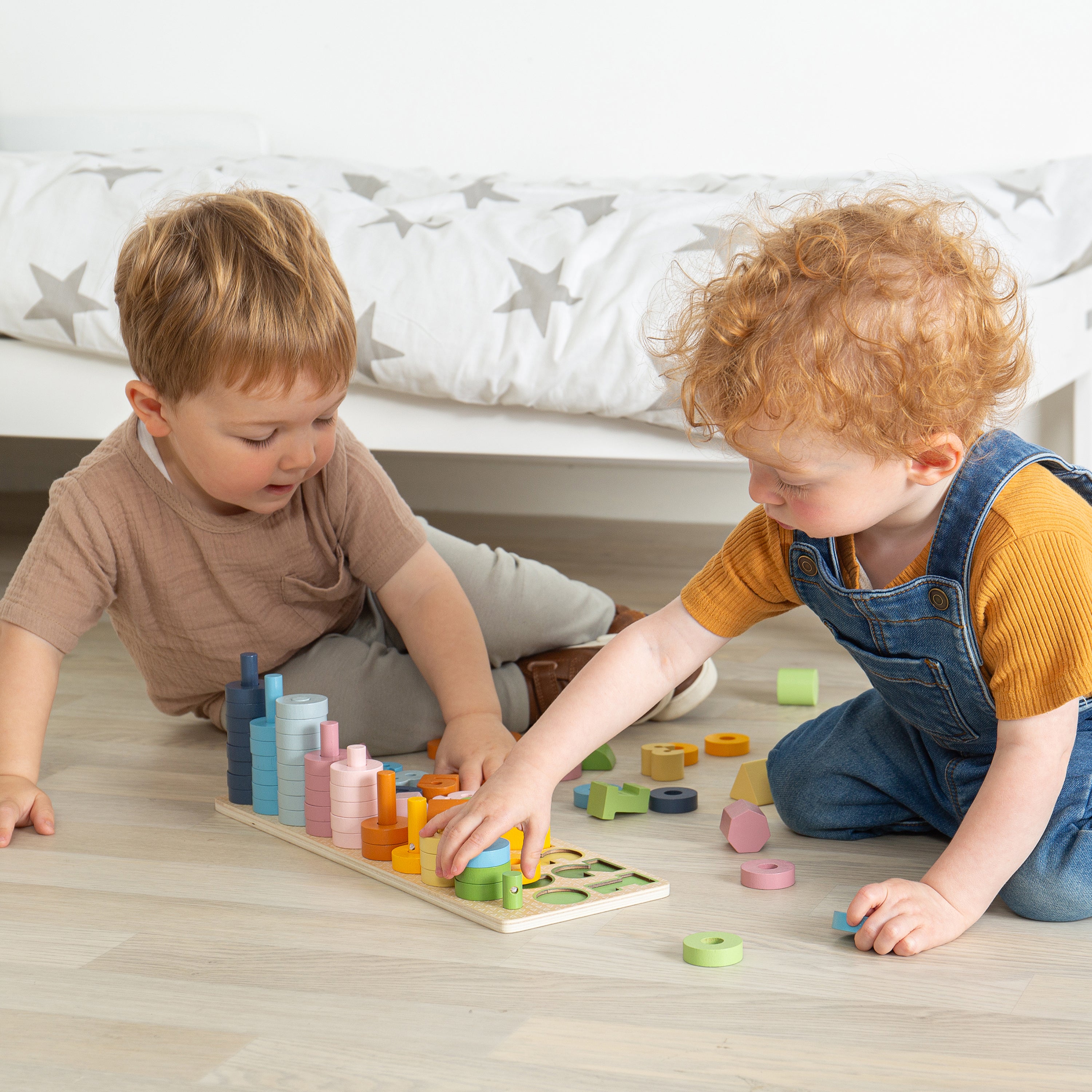 Two children playing with colorful building blocks on a wooden floor.