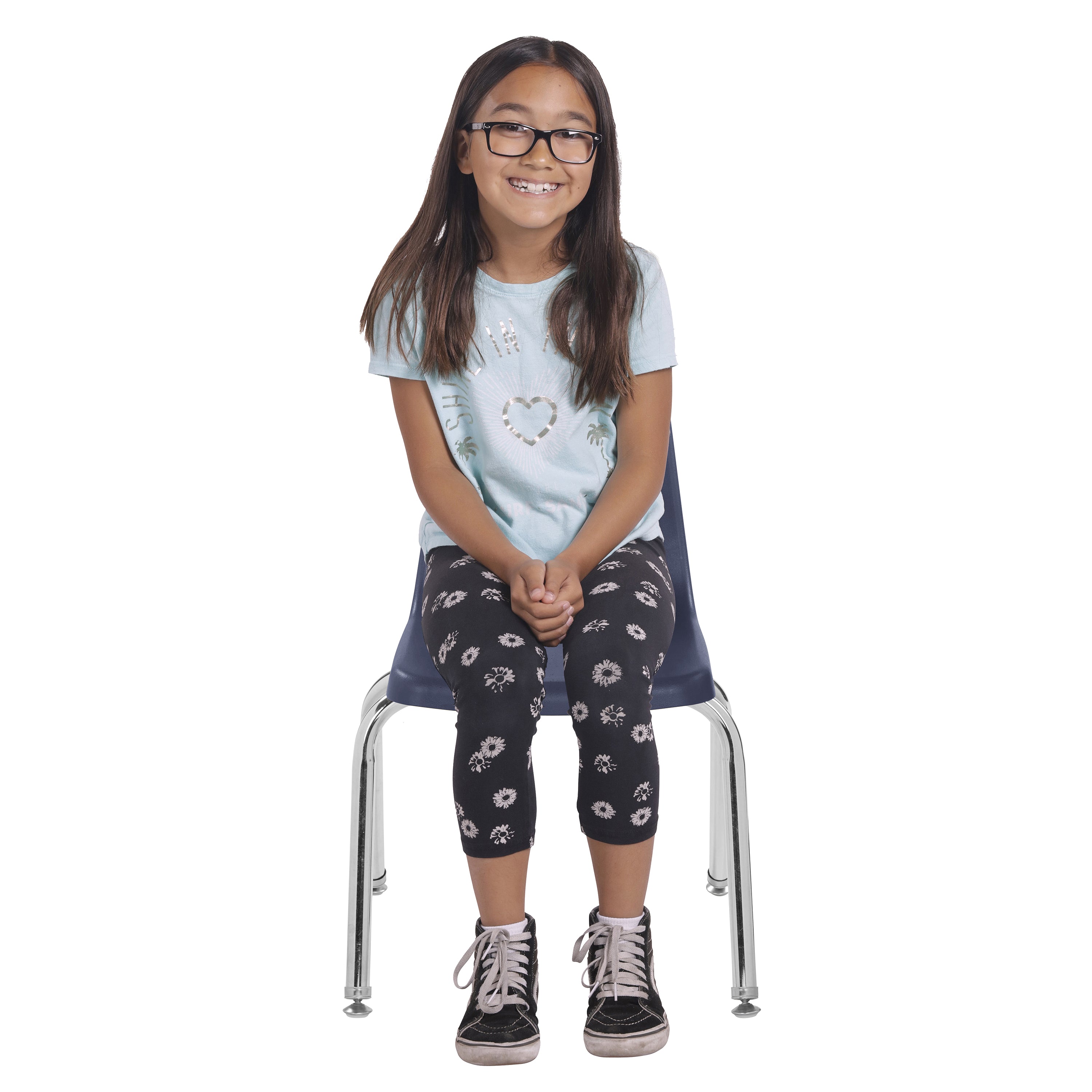 Young girl sitting on a chair wearing glasses, a light blue shirt, and dark floral leggings.