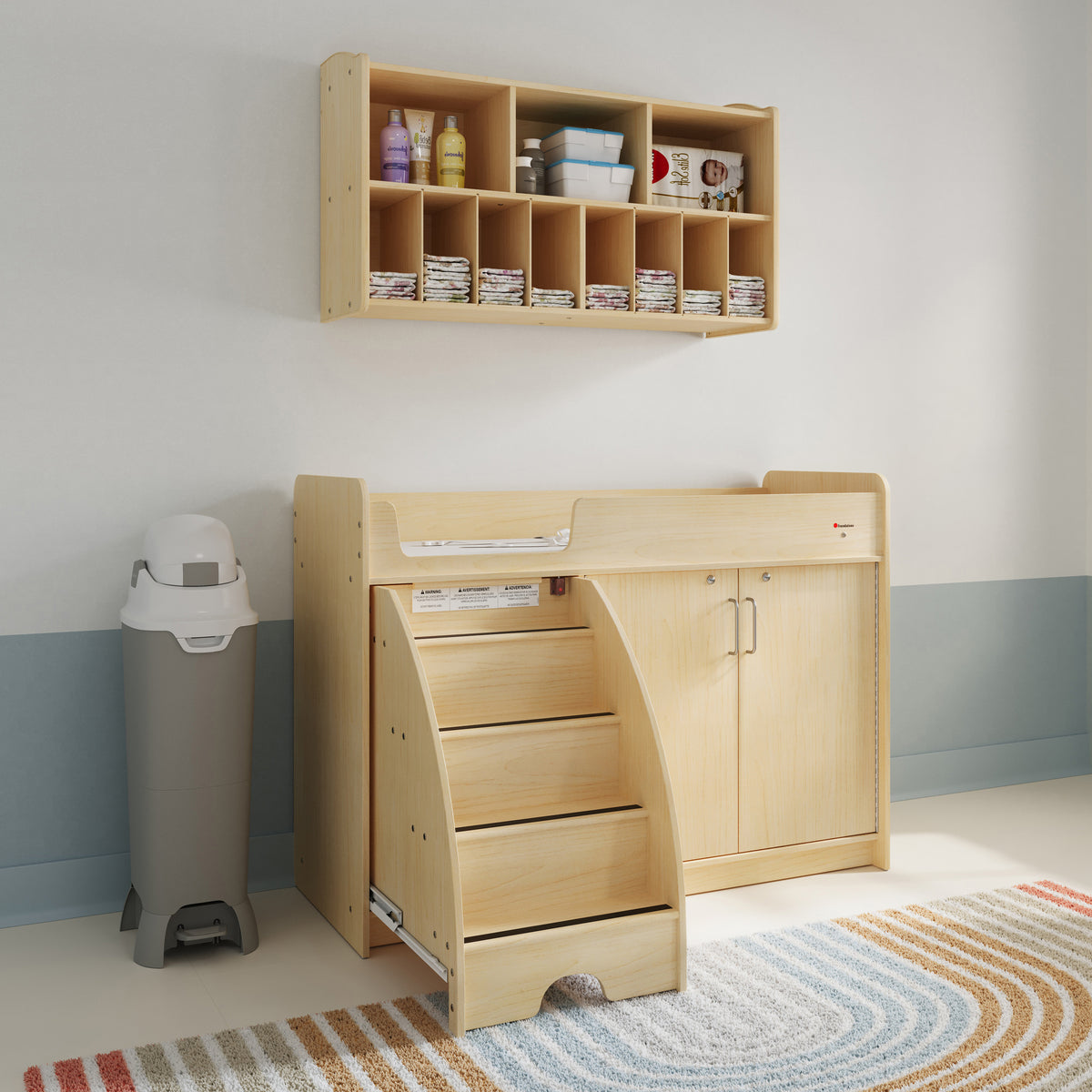 Daycare changing area with tall diaper pail beside a wooden changing station and diaper storage organizer