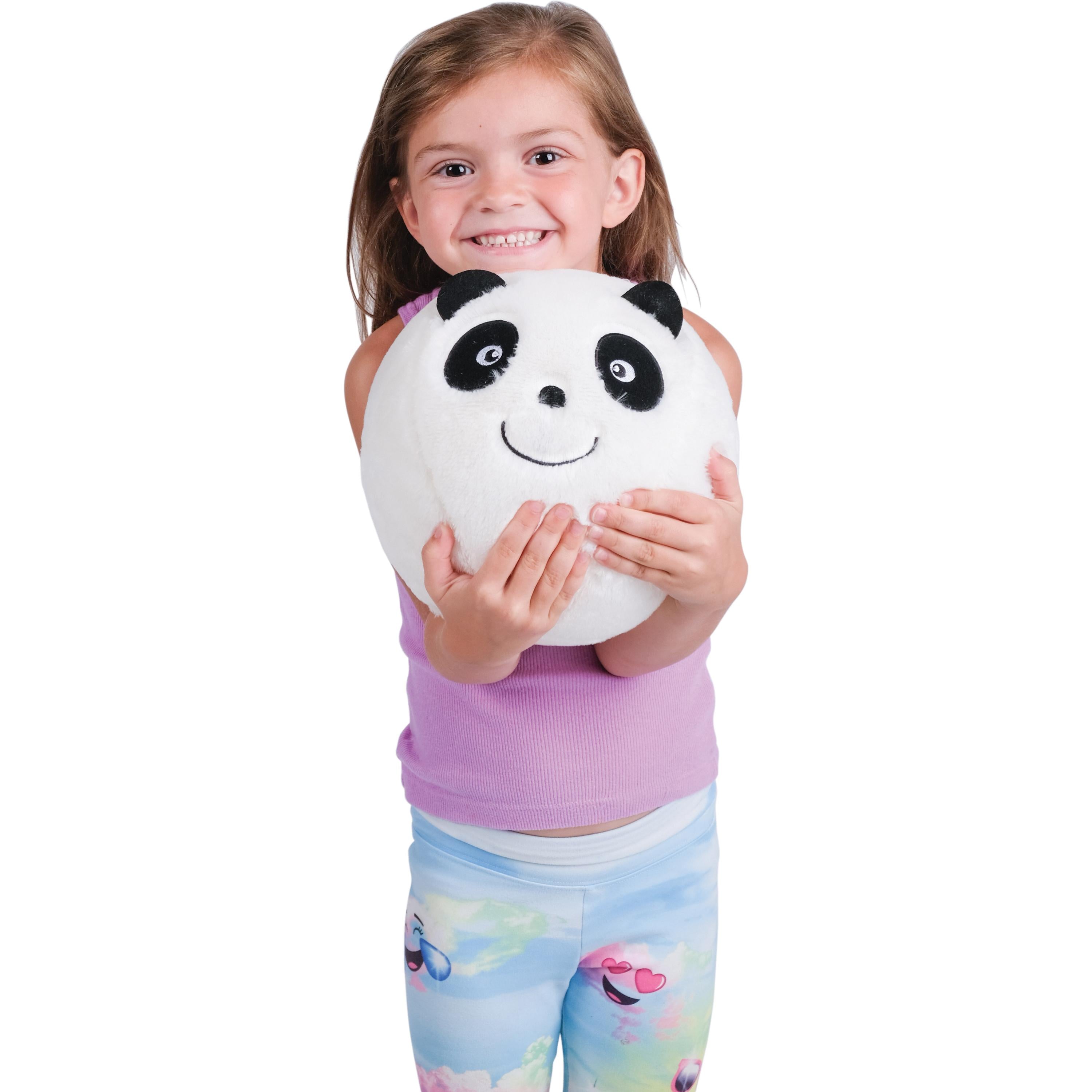 A young girl with brown hair smiling while holding a round, white plush panda toy against a solid white background.