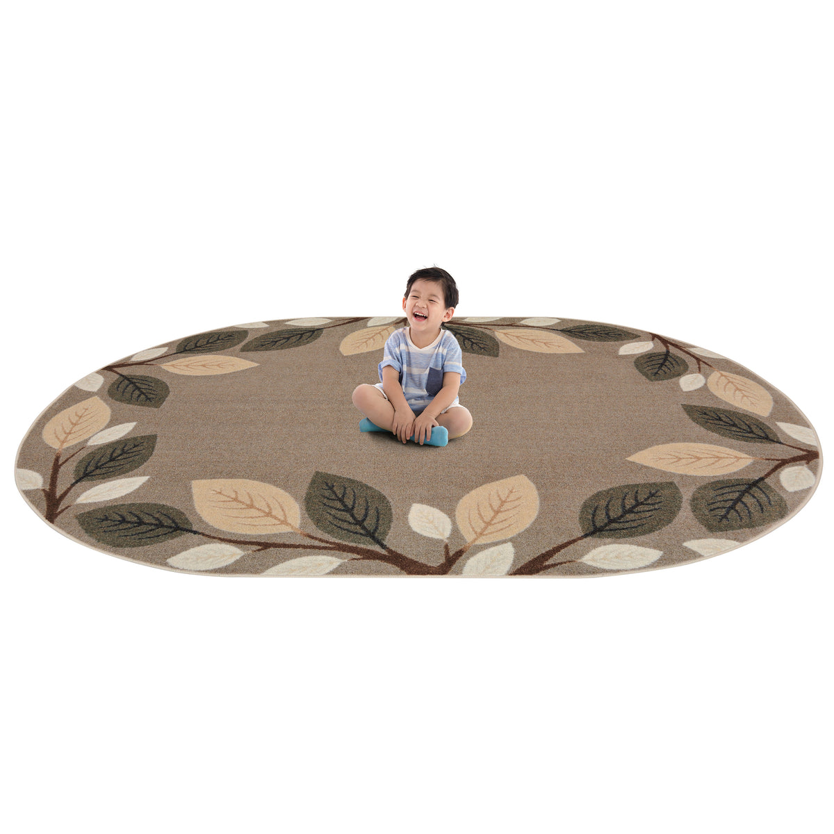 A toddler sits cross-legged in the center of a large oval area rug with a leaf pattern. The rug has a warm taupe background with branches and leaves in dark olive green, beige, and cream.