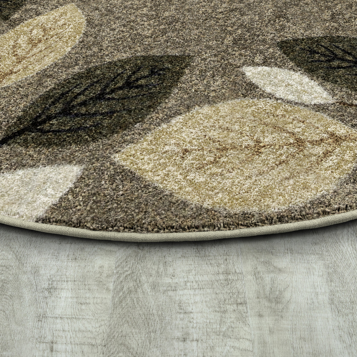 A close-up of a round area rug with a leaf pattern in shades of brown, beige, and dark olive green, shown on a light gray wood-look floor.