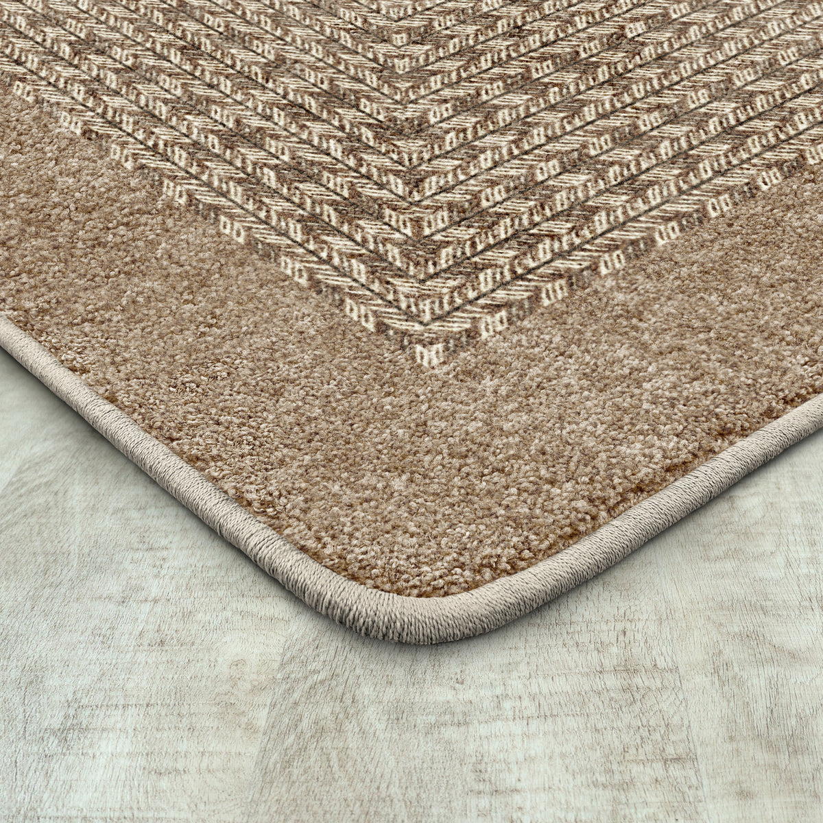 A close-up of a textured area rug corner showing a woven herringbone pattern in beige and brown tones, with a thick looped pile and a light beige edge, placed on a light gray wood-look floor.