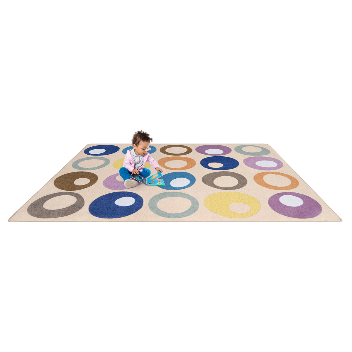 A child sits on a large rectangular play rug with a cream base and colorful concentric circle pattern in blue, purple, yellow, orange, brown, and gray, photographed on a plain white background.