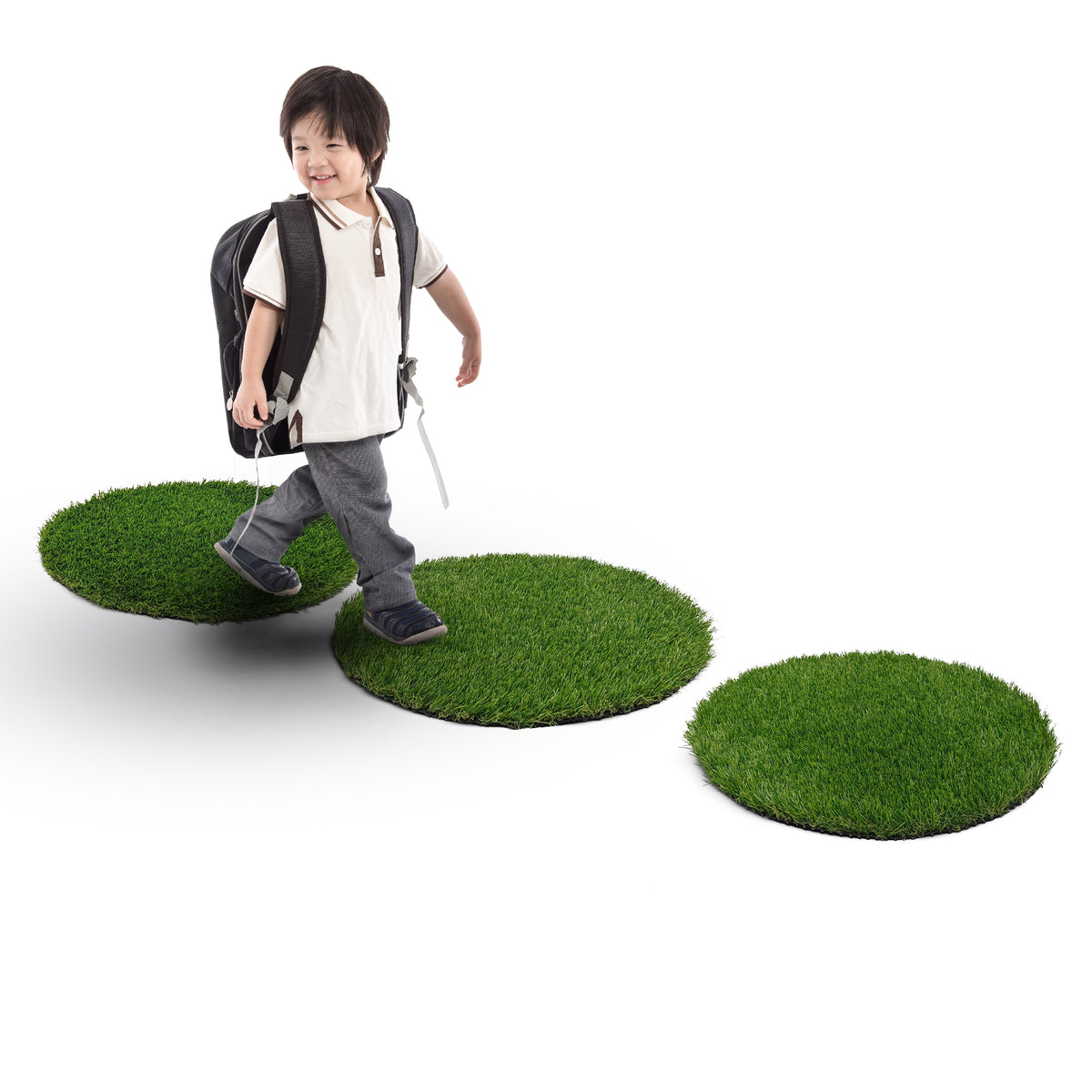 A child with a backpack standing on three round green artificial grass turf pads 
