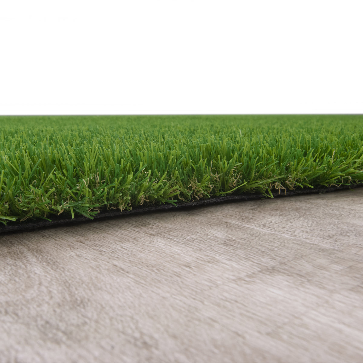 Green artificial turf grass with a black backing layer shown on a light gray textured surface against a white background.