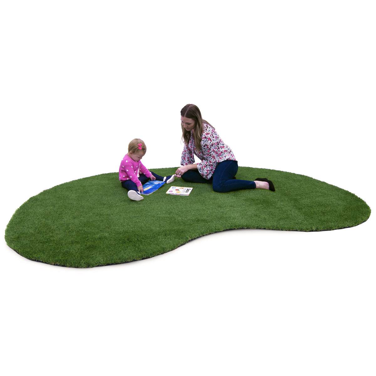 A toddler and adult woman sit on a large, organic-shaped green artificial turf rug against a solid white background.
