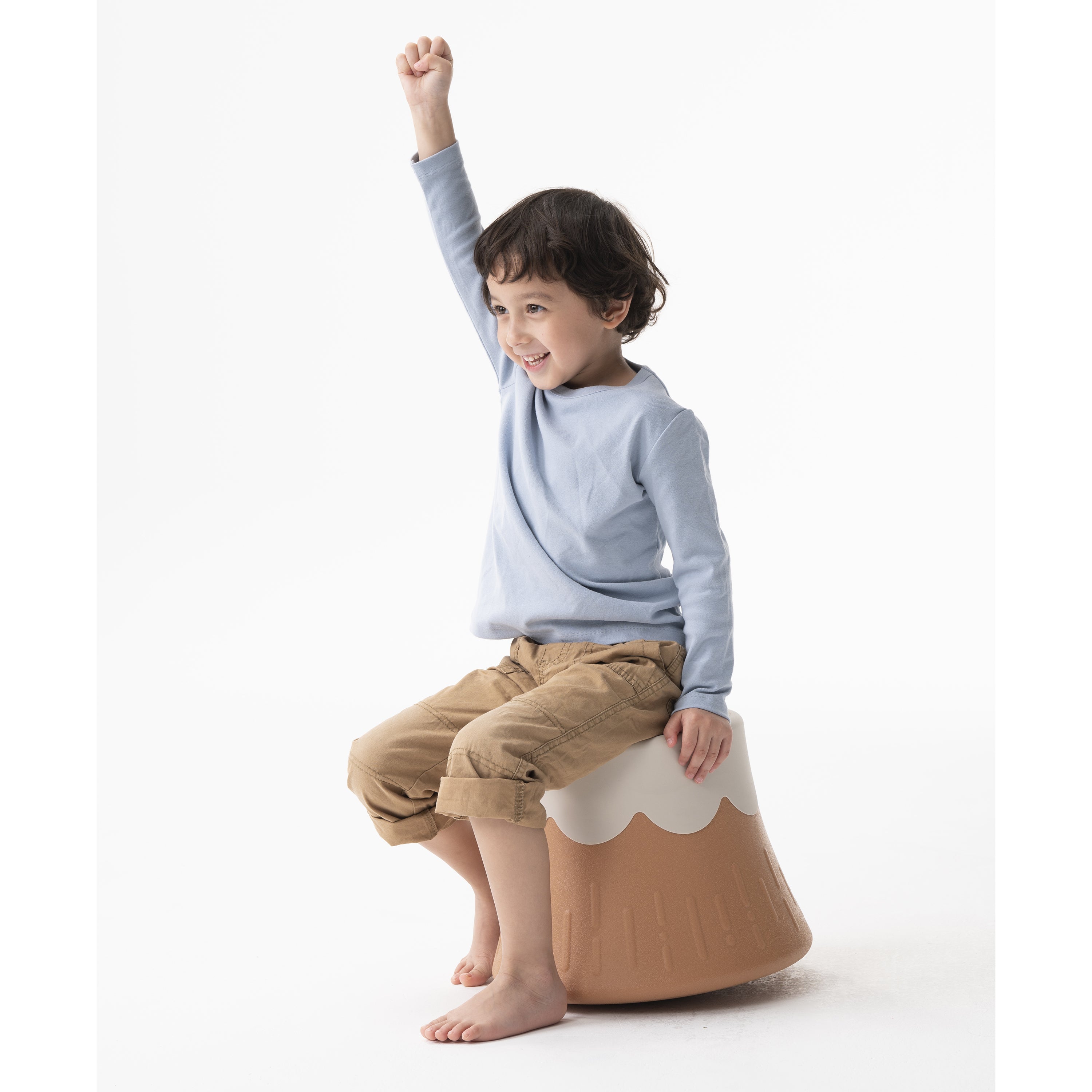 Child sitting on a brown and white stool with one leg raised on a white background