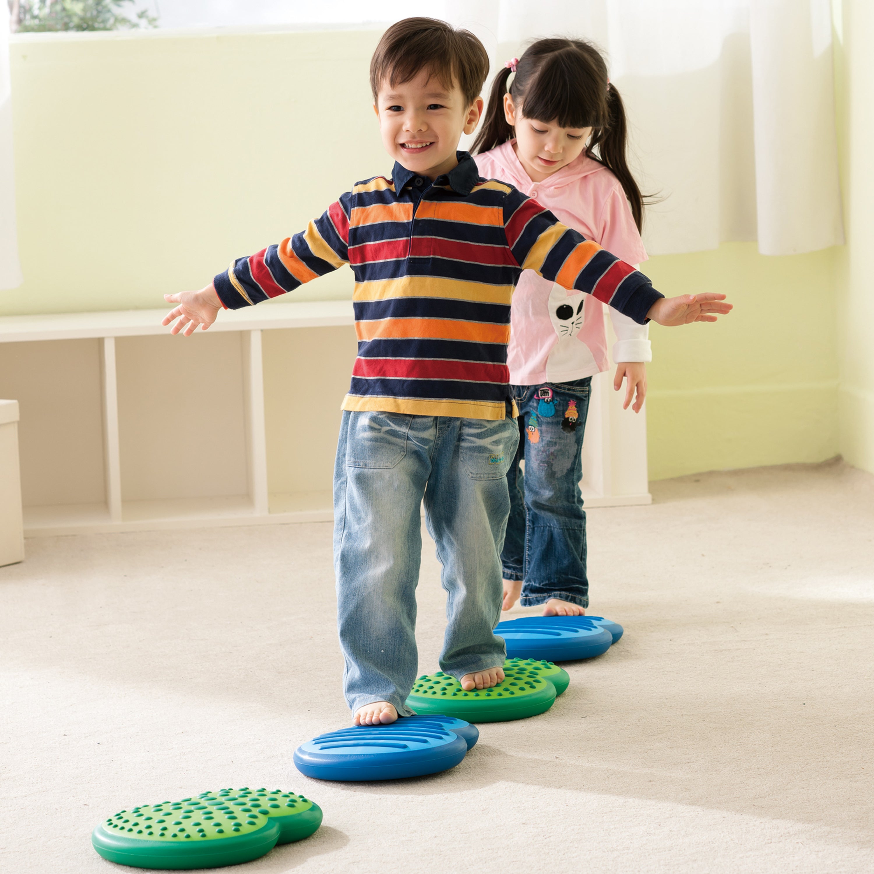 Two children standing on colorful stepping stones indoors.