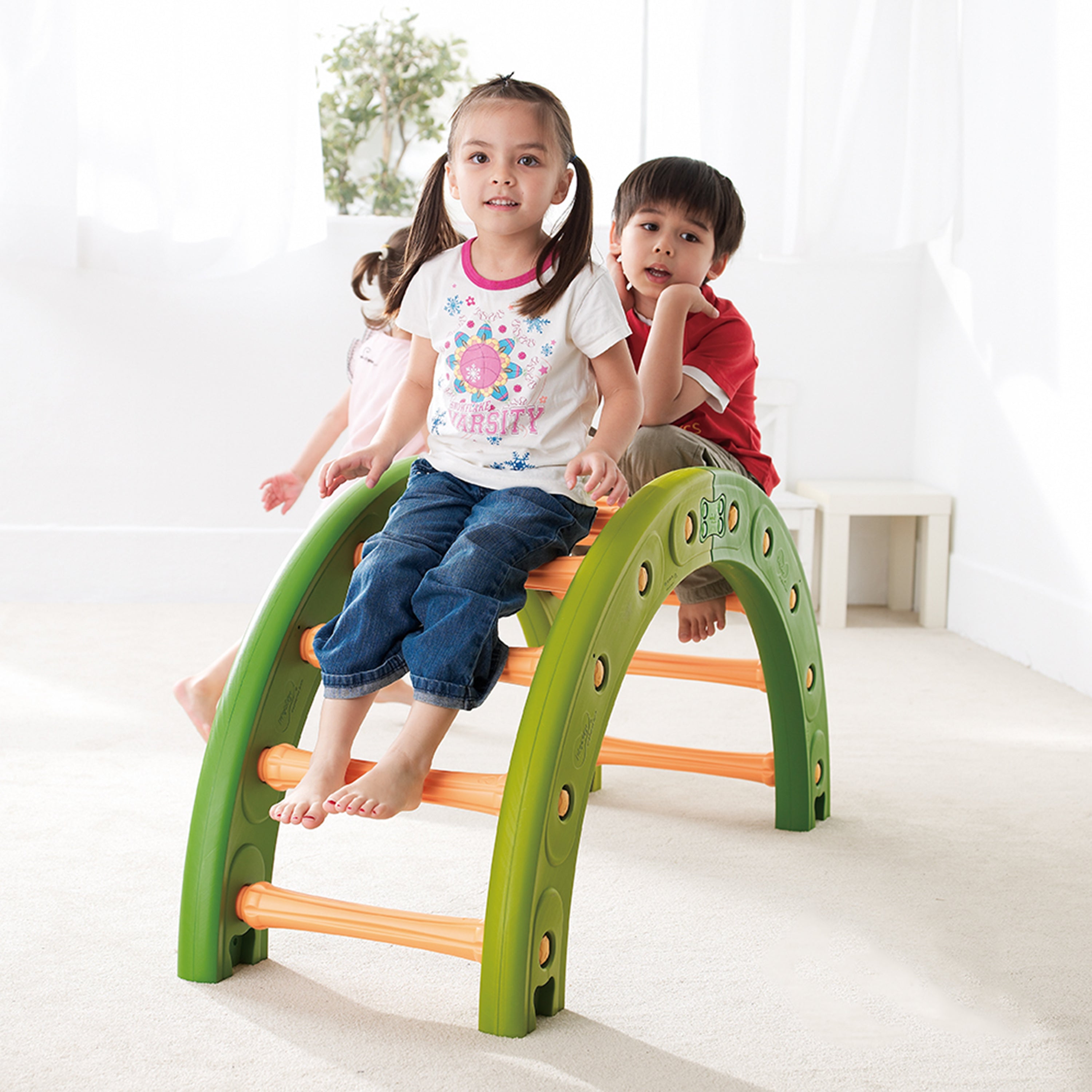 Children playing on a green and orange playground structure indoors.