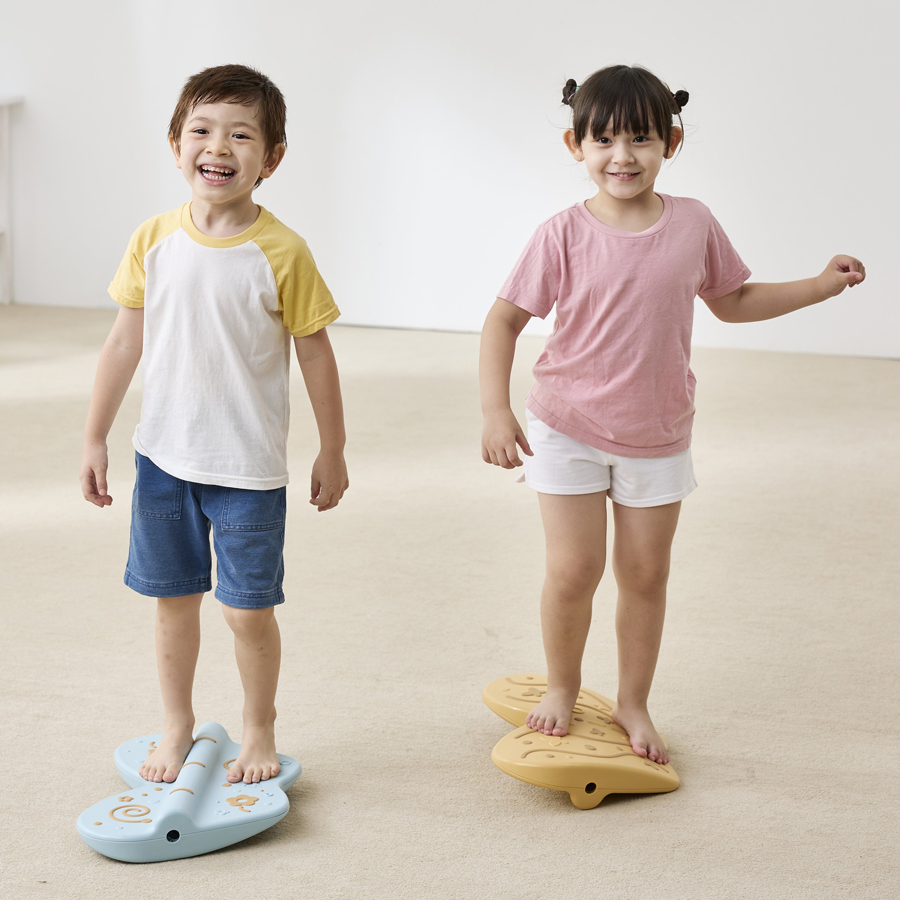 Two children standing on balance boards in a room with a white wall.