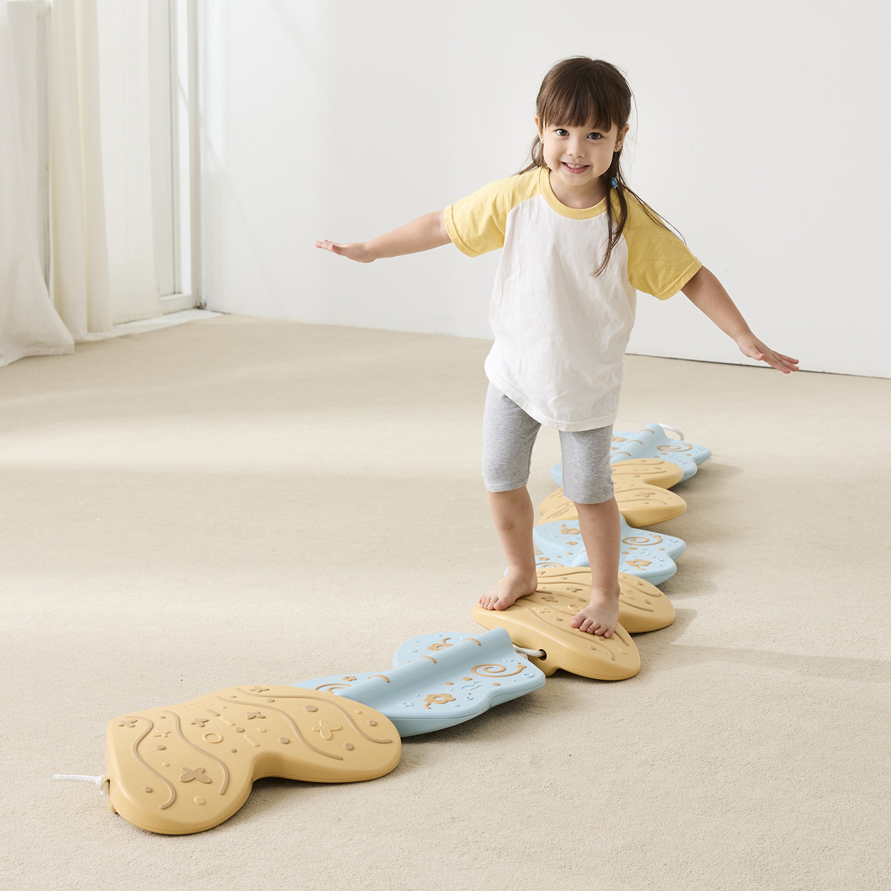 Child standing on a series of stepping stones in a room with white walls and beige carpet.