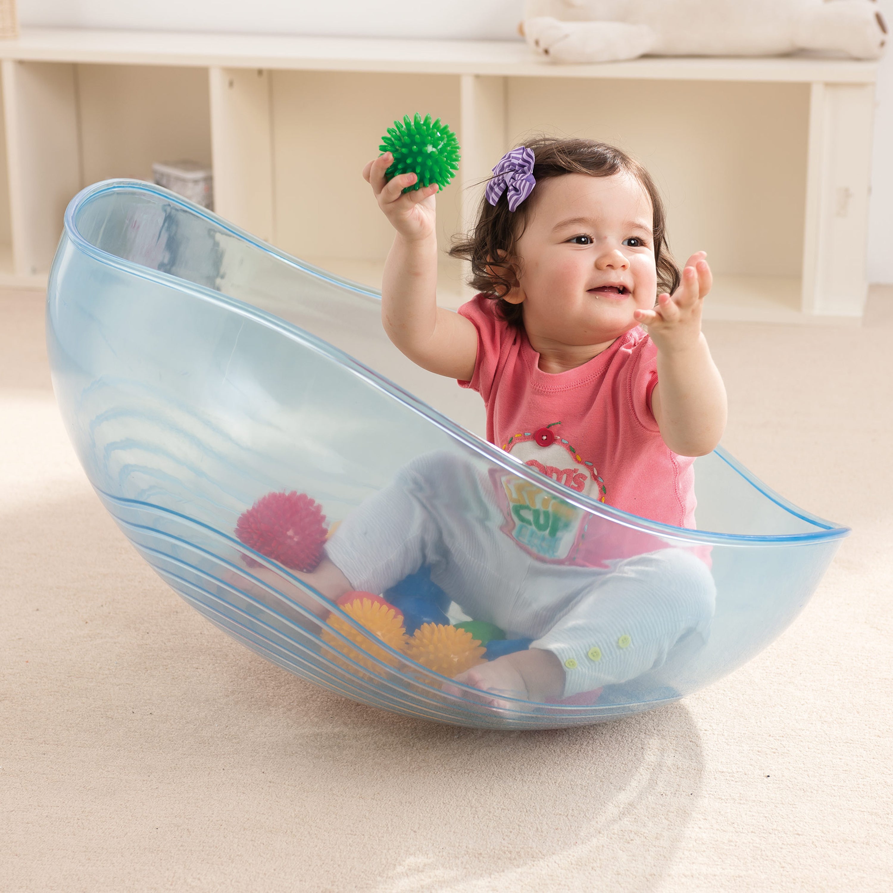 Child playing with colorful toys inside a transparent blue plastic ball pit.