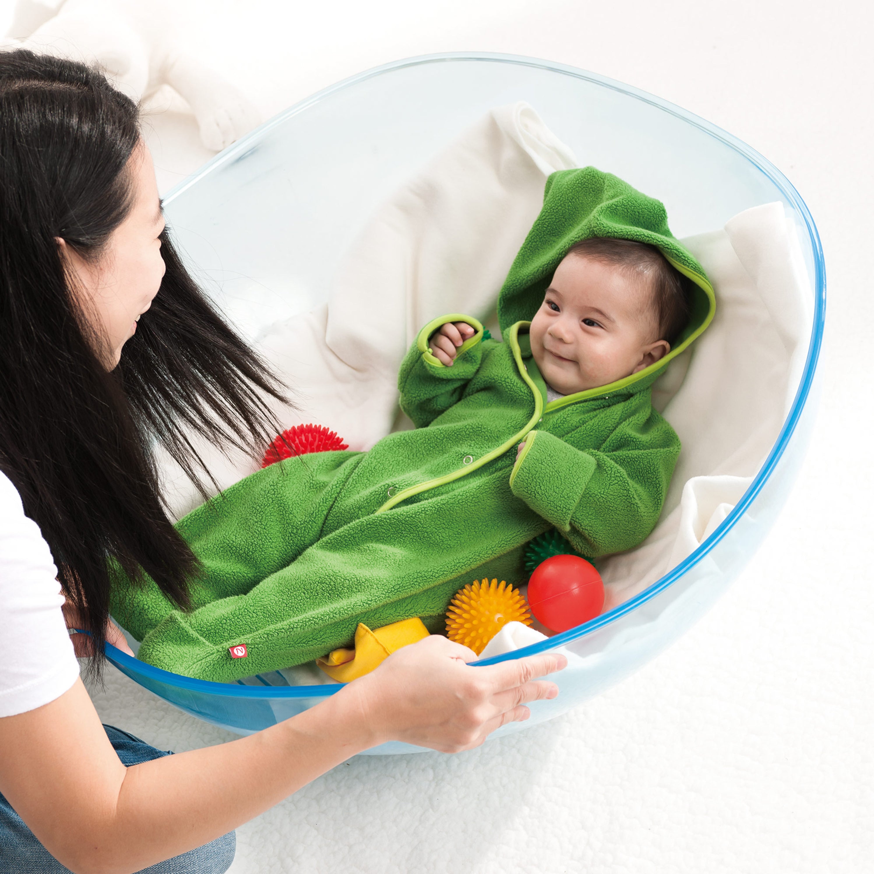 Baby in a green outfit playing with colorful toys in a baby bouncer.