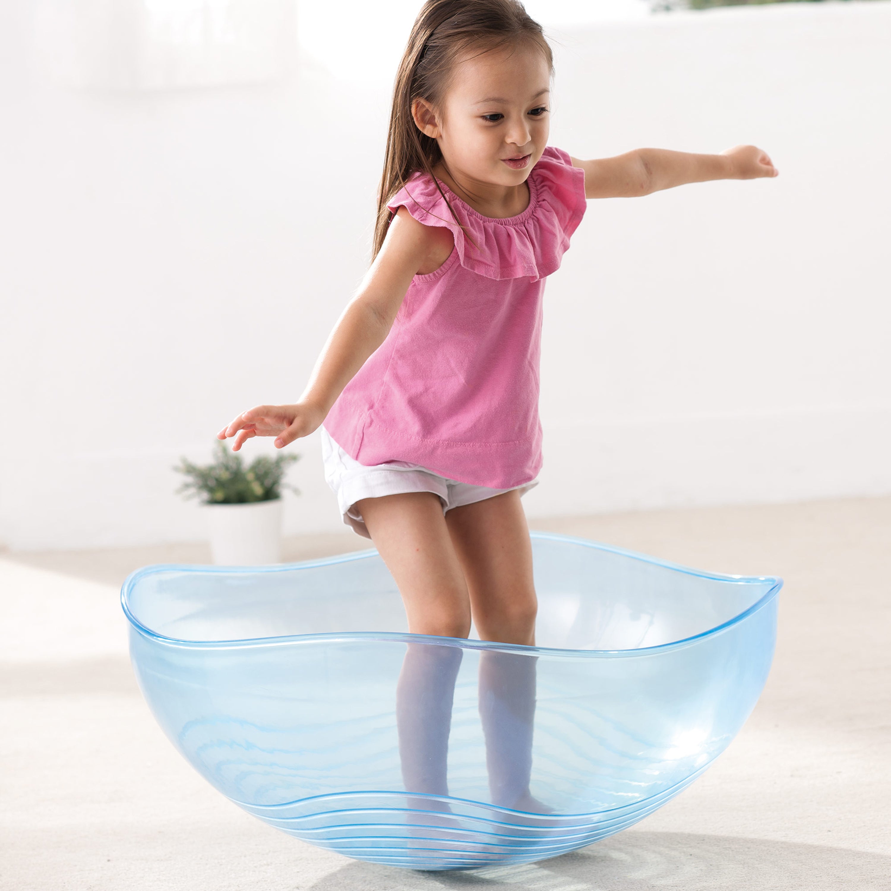 Child playing inside a large blue plastic bowl on a light background