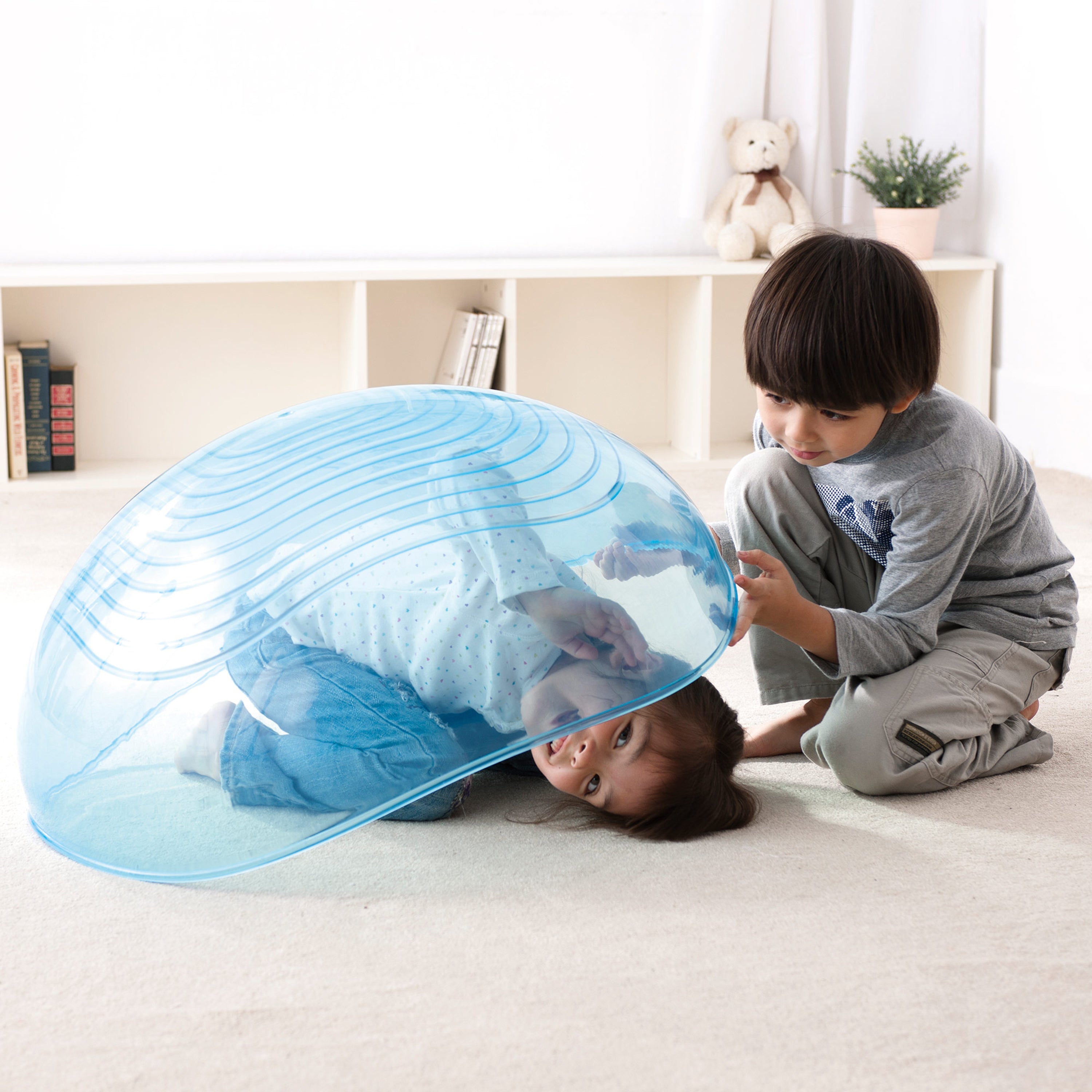 Two children playing with a blue inflatable dome toy on a light-colored floor.