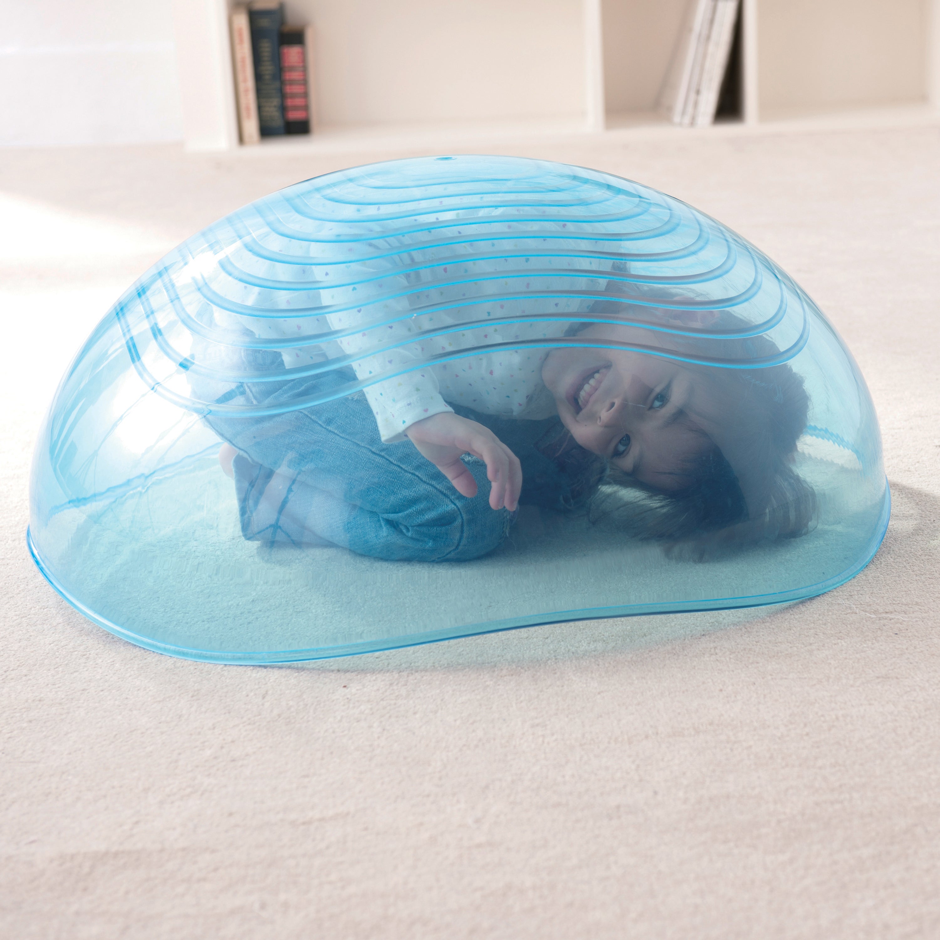Person lying inside a transparent blue inflatable dome on a white surface.