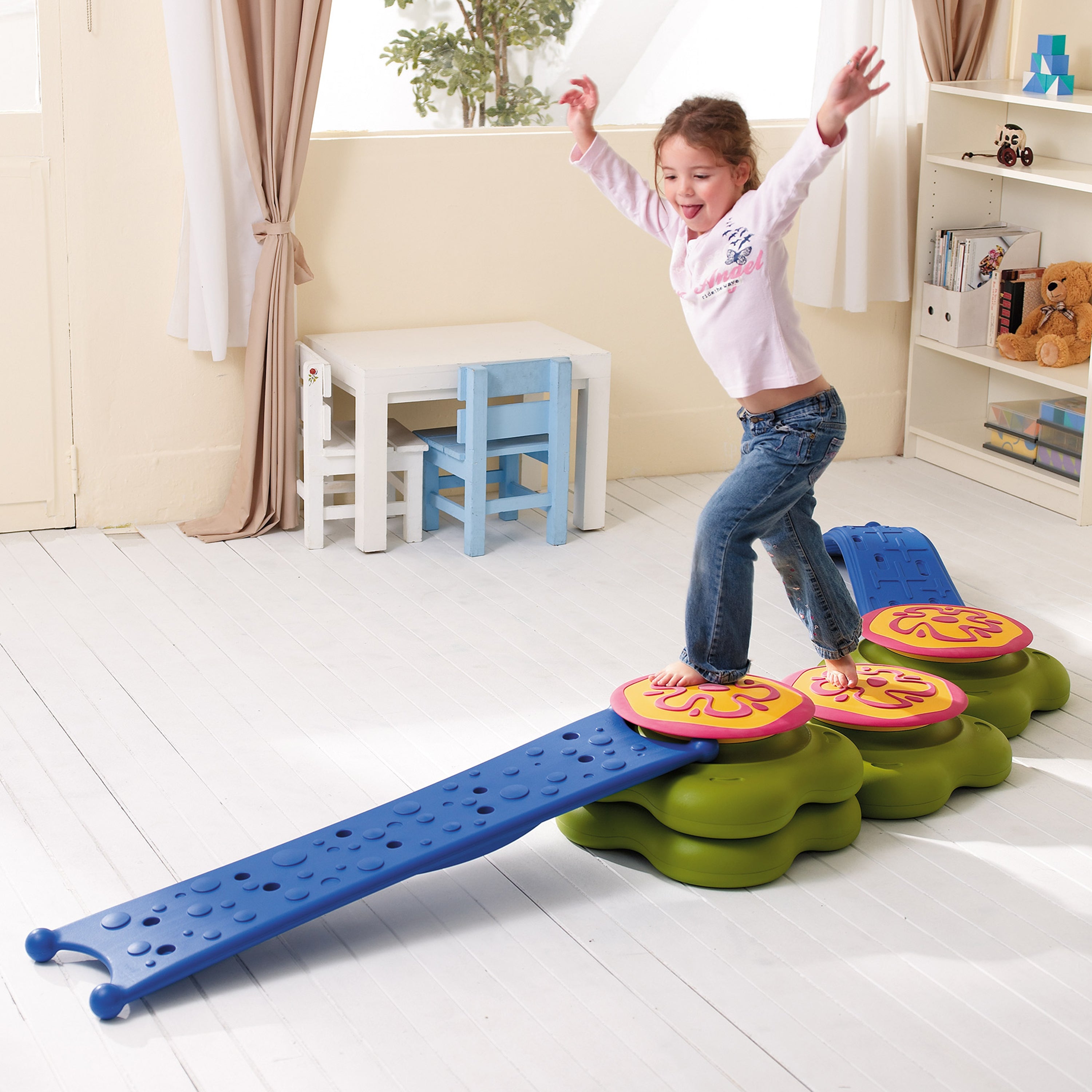 Child playing on a colorful balance beam toy in a room with furniture and decor.