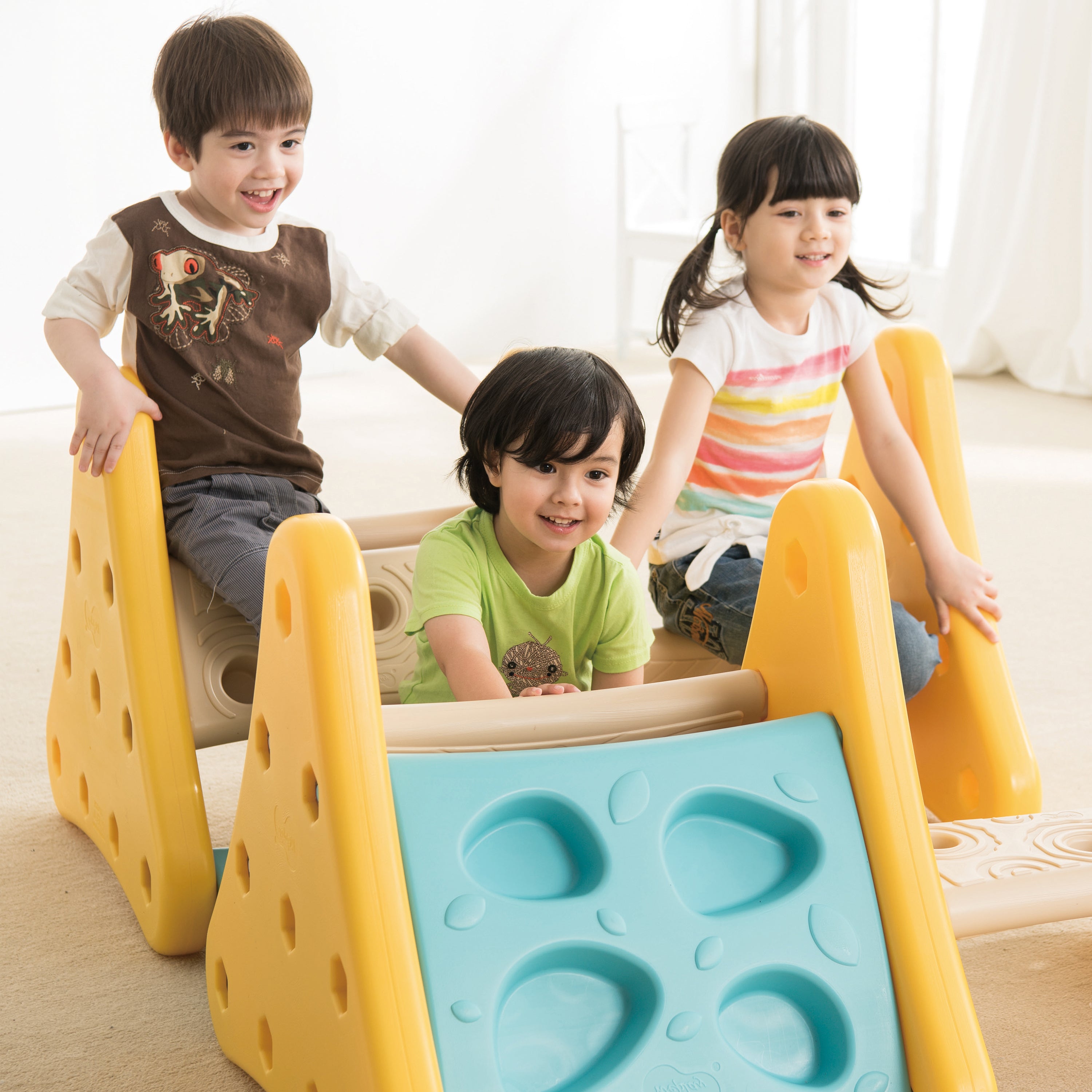 Three children playing on a colorful climber indoors.