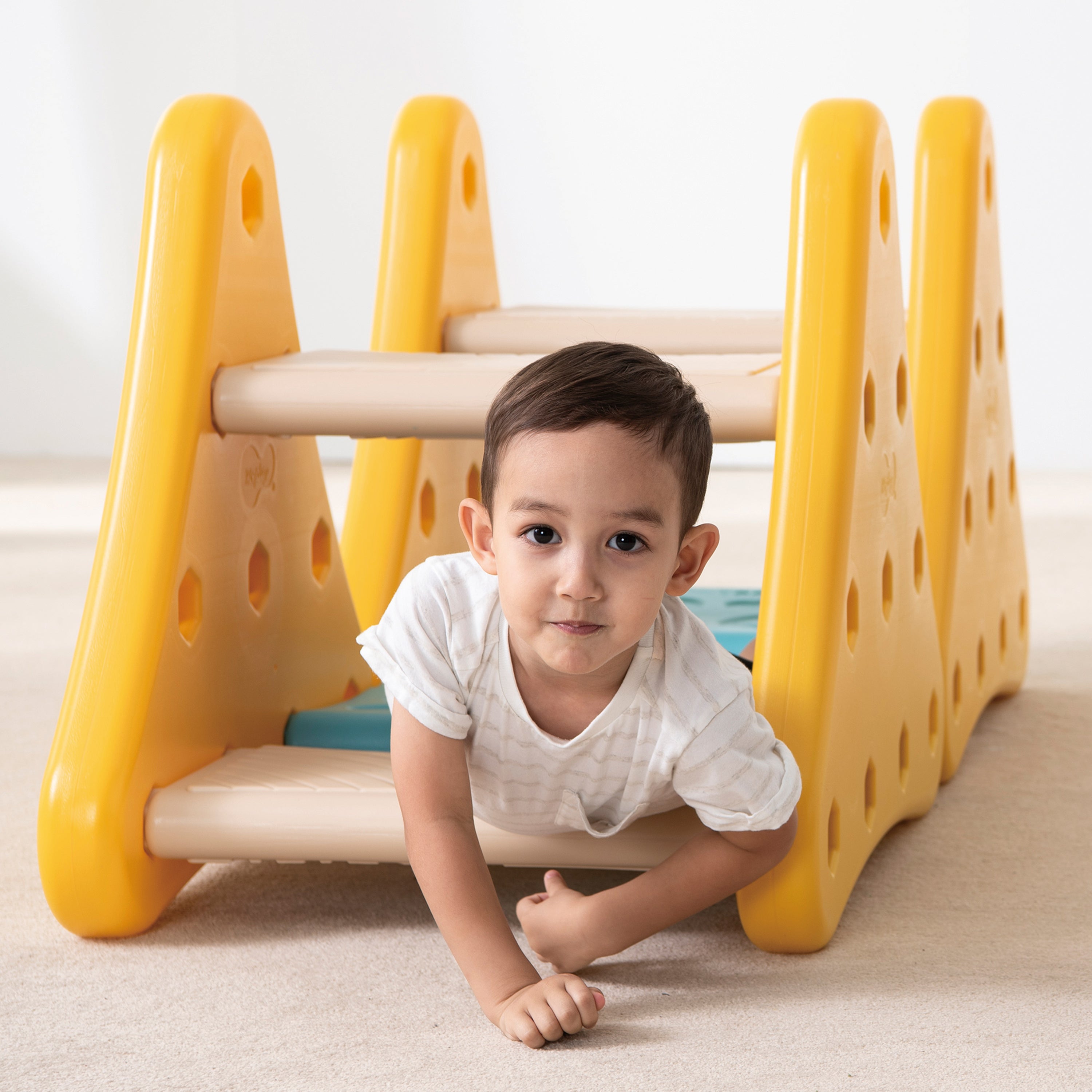 Child playing with a yellow and beige playground structure on a light-colored floor.