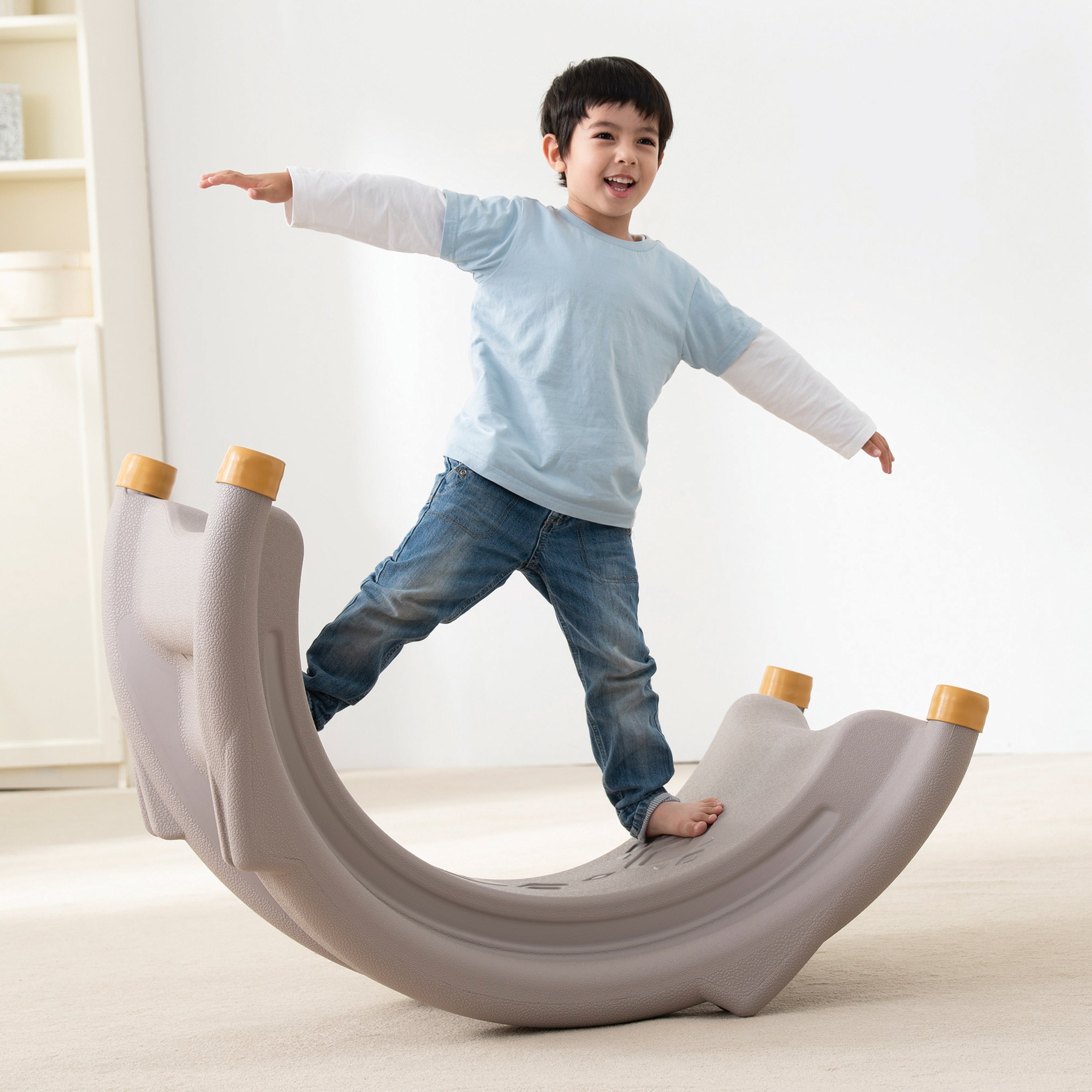 Child playing on a large, curved, gray playground structure in a bright room.